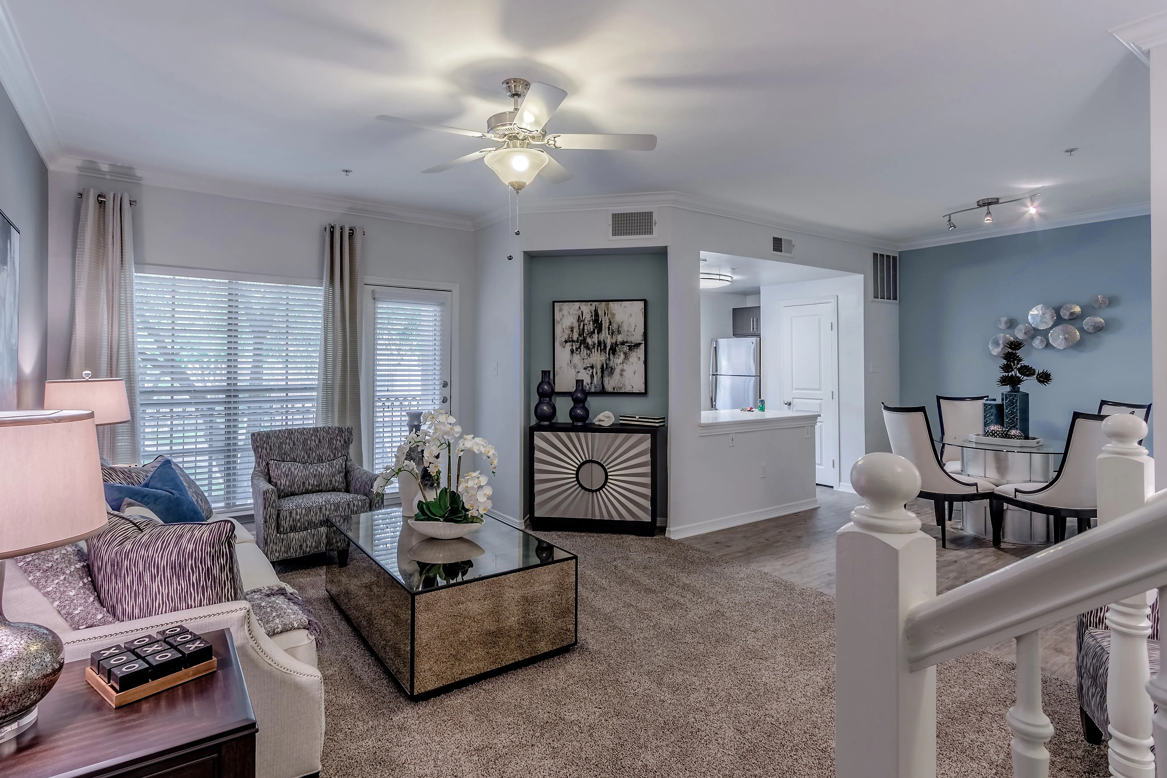 Elegant open-concept living room with cozy seating, sleek glass coffee table, and modern dining area. Bright kitchen view enhances the spacious ambiance.