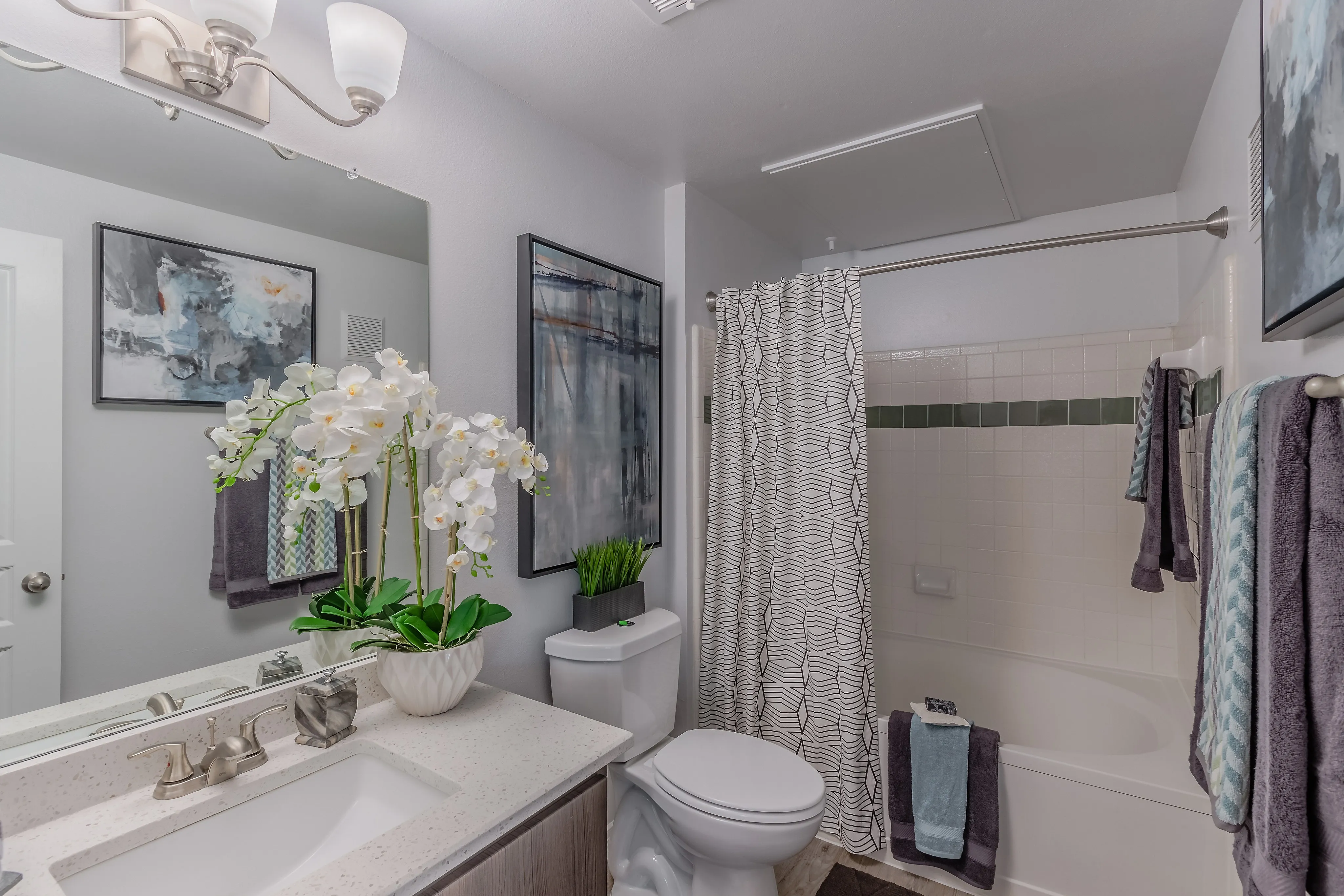 Elegant bathroom featuring modern fixtures, vibrant artwork, plush towels, and a stylish vanity with decorative orchids for a tranquil atmosphere.