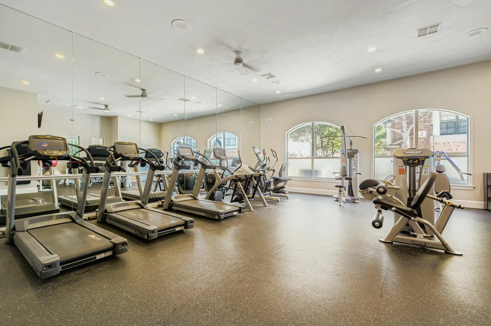 Luxury apartment gym featuring modern treadmills, workout machines, and full-length mirrors in a well-lit, spacious environment.