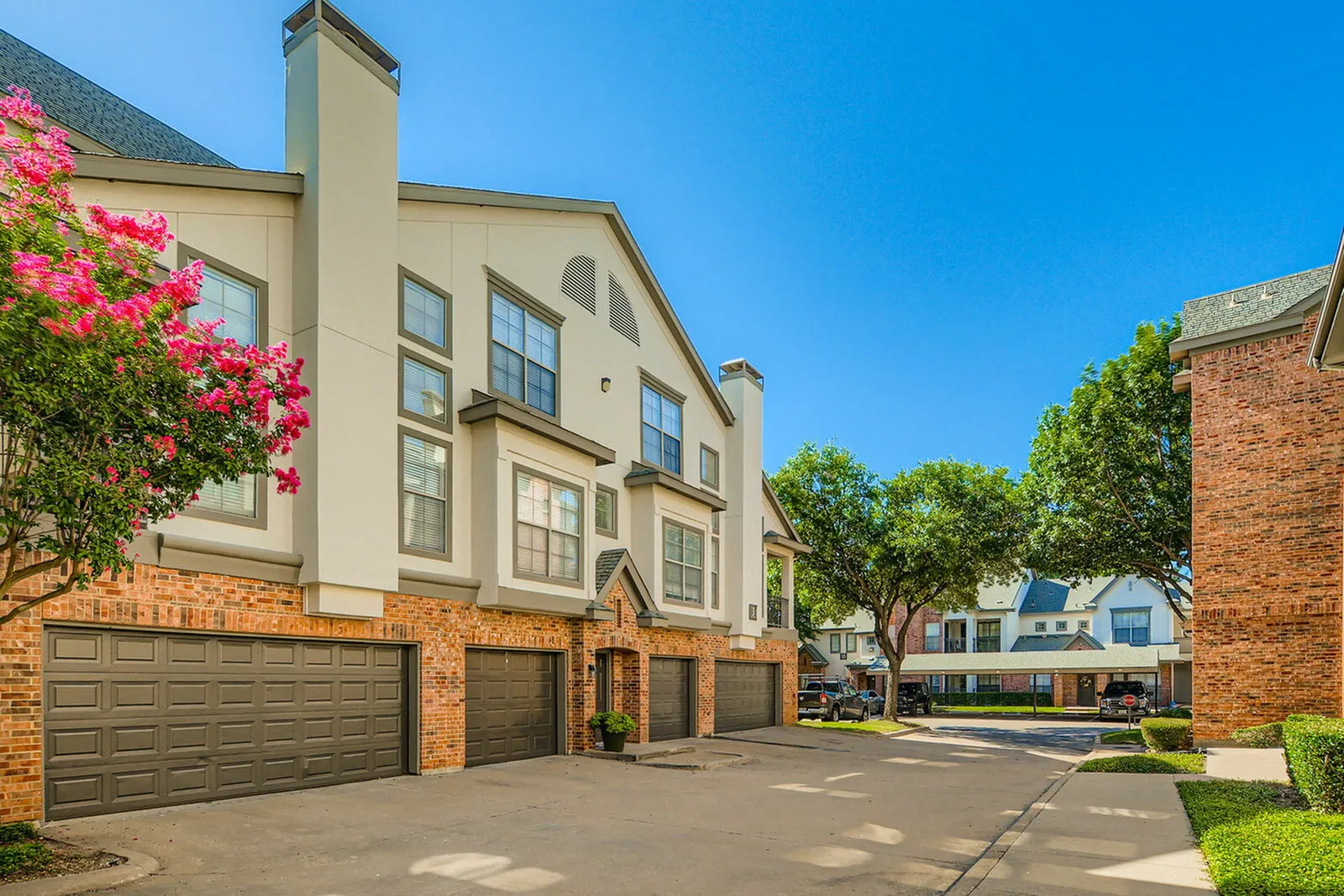 Charming residential complex with modern architecture, featuring brick accents and lush trees under a clear blue sky.