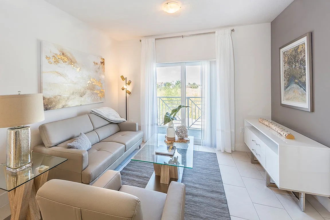 Bright and modern living room with stylish decor, large glass doors, and a cozy seating area leading to a sunny balcony view.