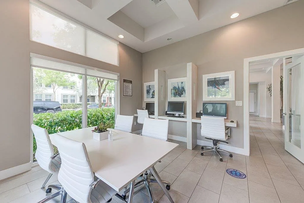 Chic and modern office space with sleek white furniture, abundant natural light, and lush greenery visible through large windows.