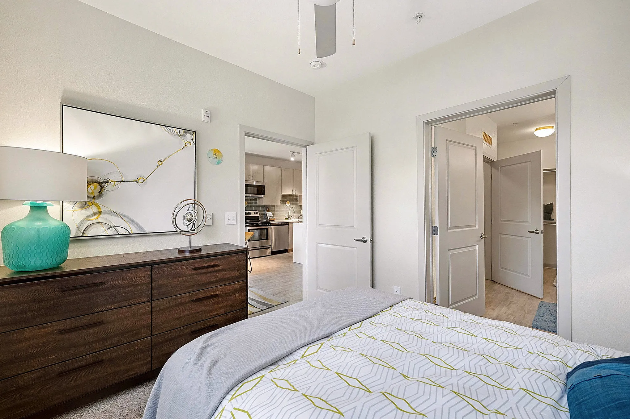 Inviting bedroom with modern decor, featuring a cozy bed, abstract art, and natural light through large windows.