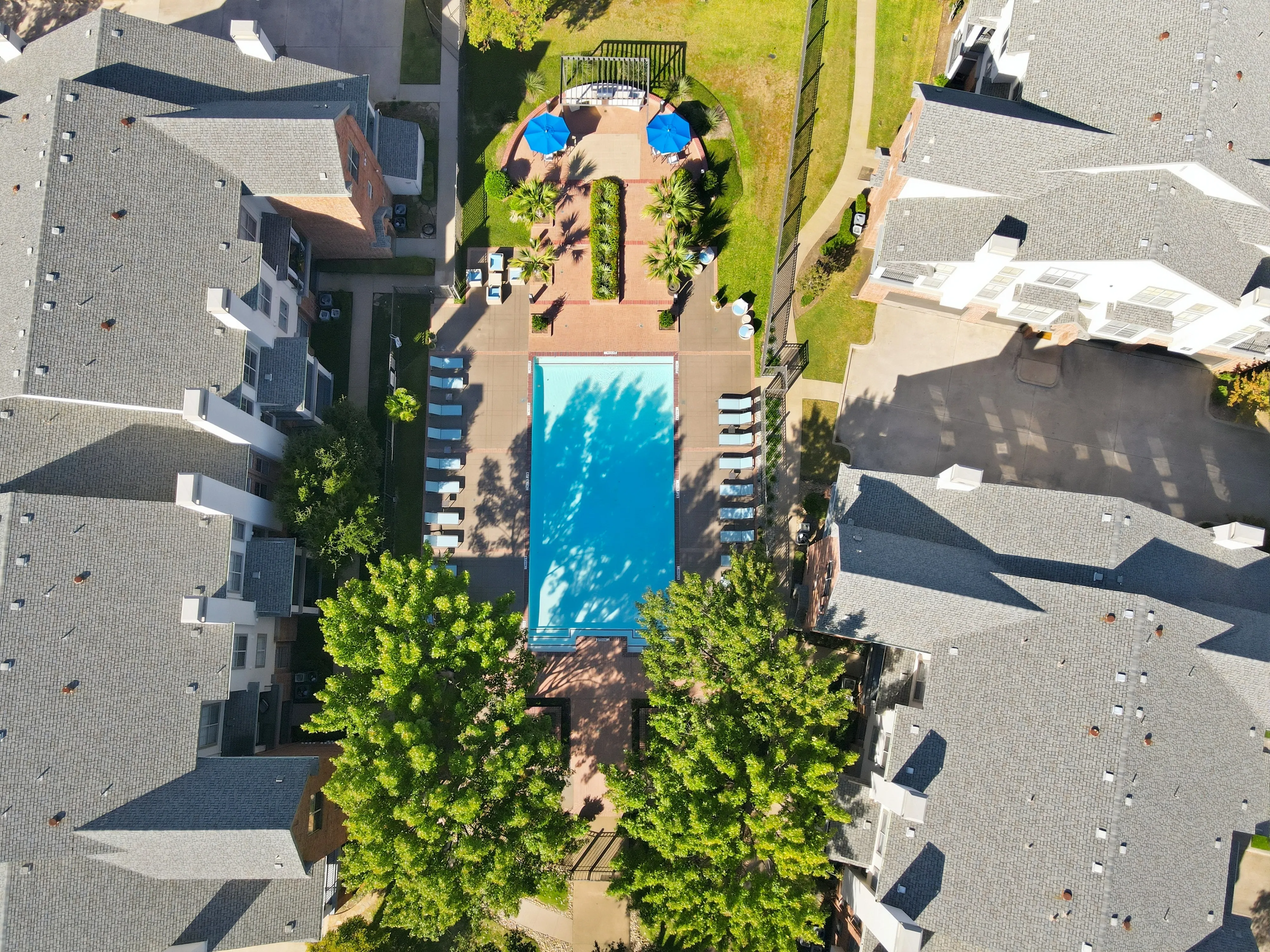 Charming apartment complex with a pristine outdoor pool area, surrounded by lush greenery and modern sun loungers.