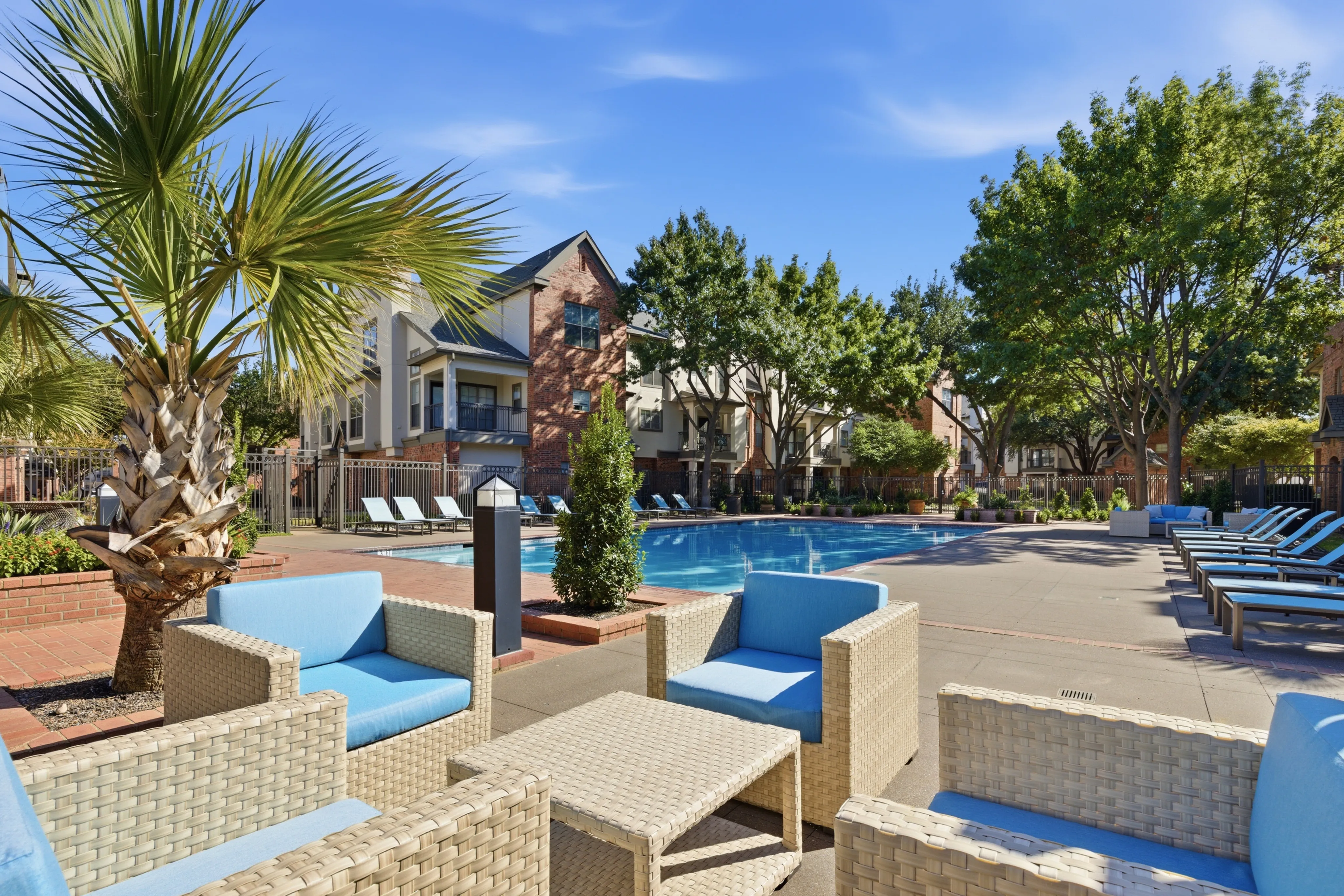 Luxurious apartment community featuring a sparkling pool, tropical landscaping with palm trees, and modern lounge areas for relaxation.