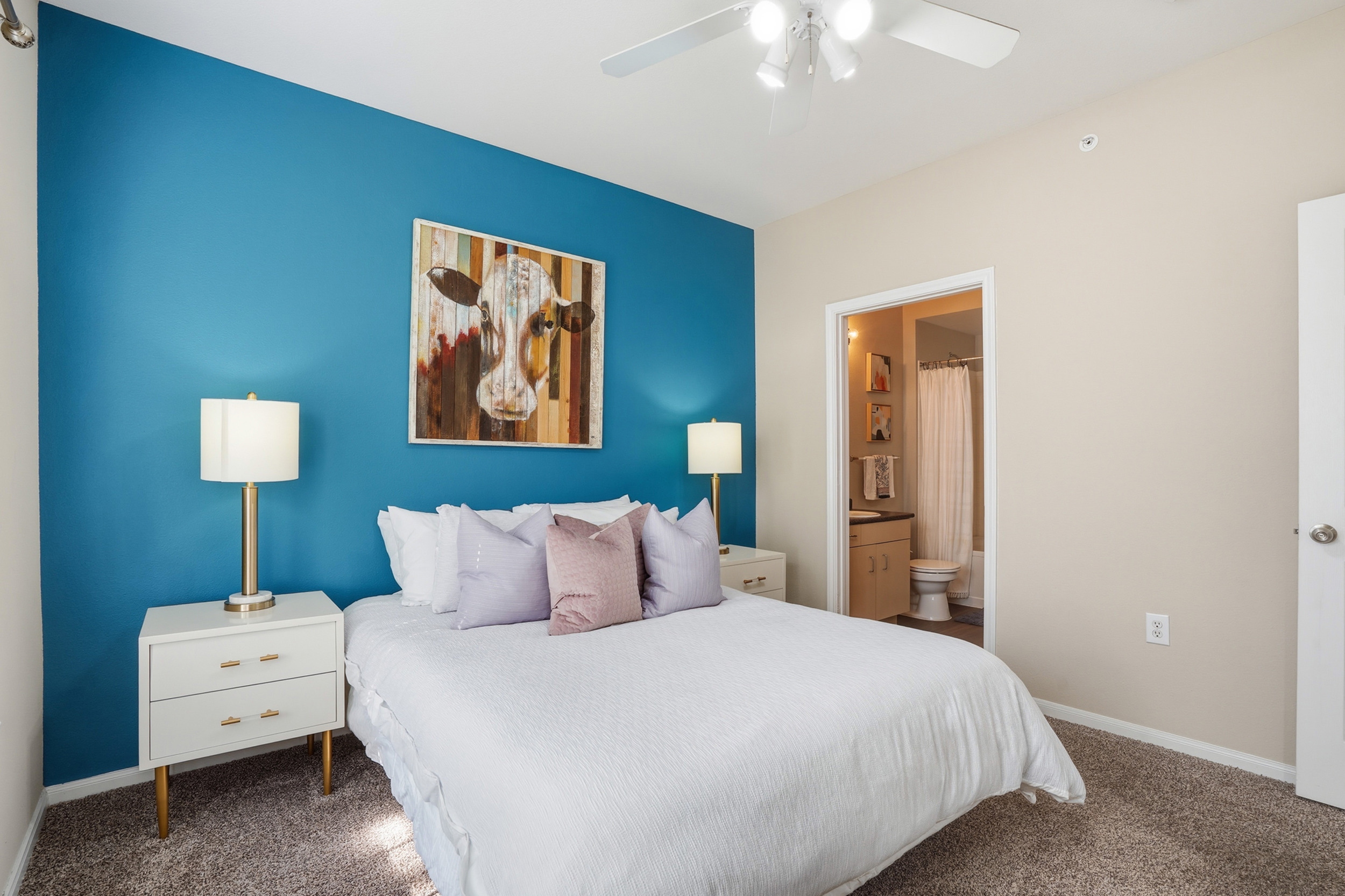 Cozy bedroom with elegant bedding and warm lighting, adjoining a modern en-suite bathroom and charming hallway.