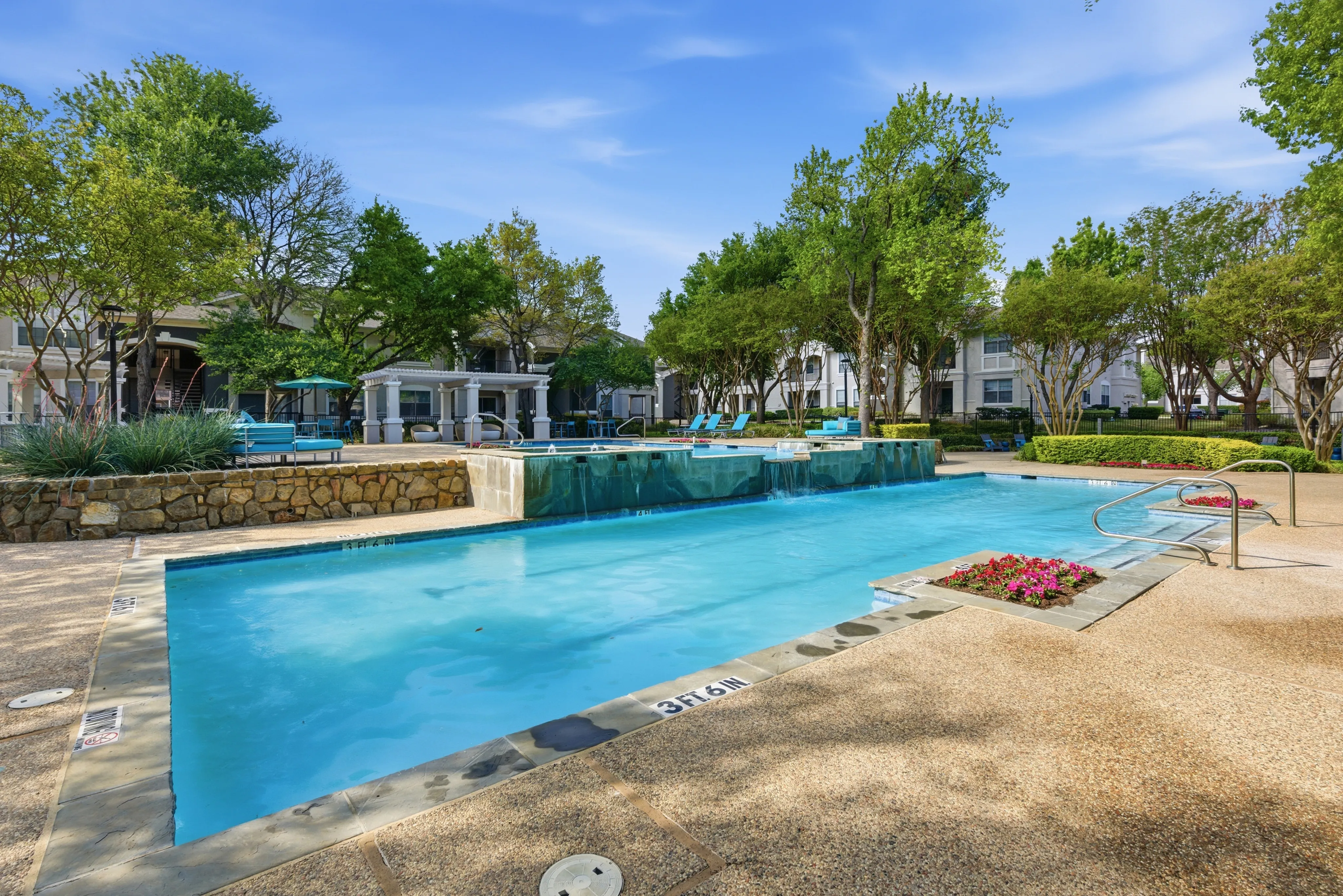 Inviting outdoor oasis with a sparkling pool surrounded by lush greenery and charming stonework, perfect for relaxation and leisure.