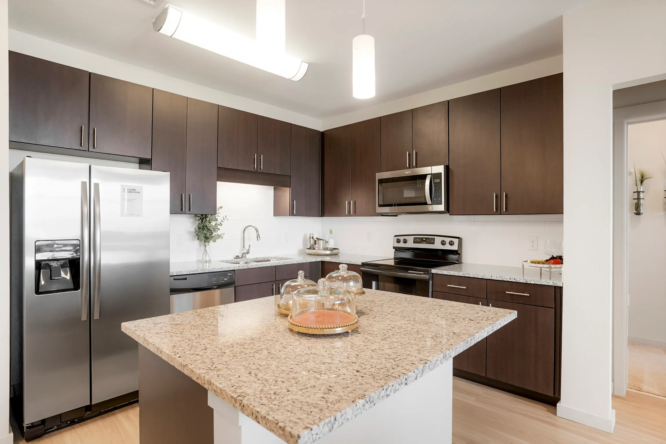 Modern kitchen featuring sleek dark wood cabinets, granite countertops, and stainless steel appliances, opening into a stylish dining area for luxurious living.