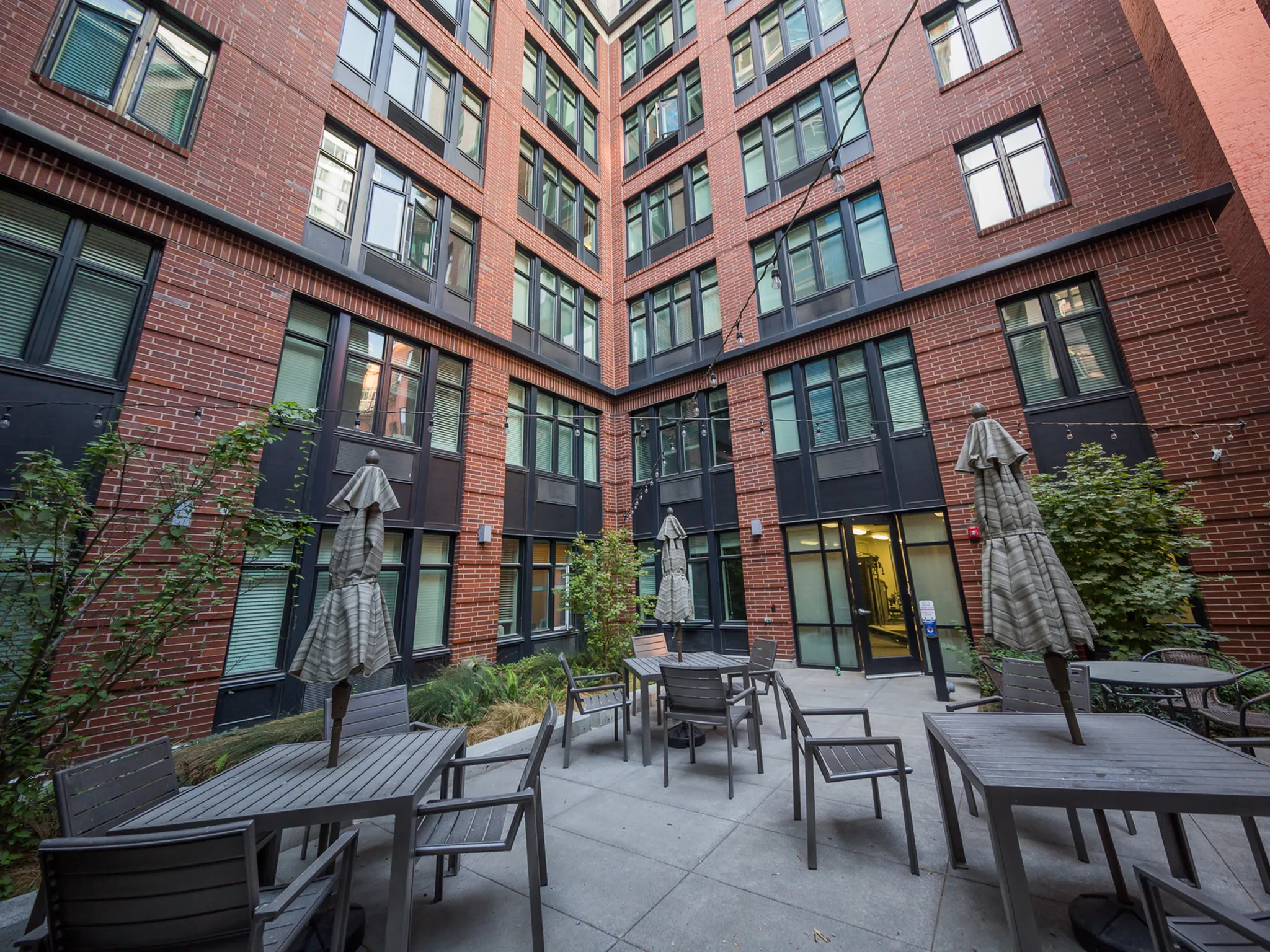 Charming urban courtyard with stylish patio furniture, surrounded by modern brick apartment building boasting large windows.