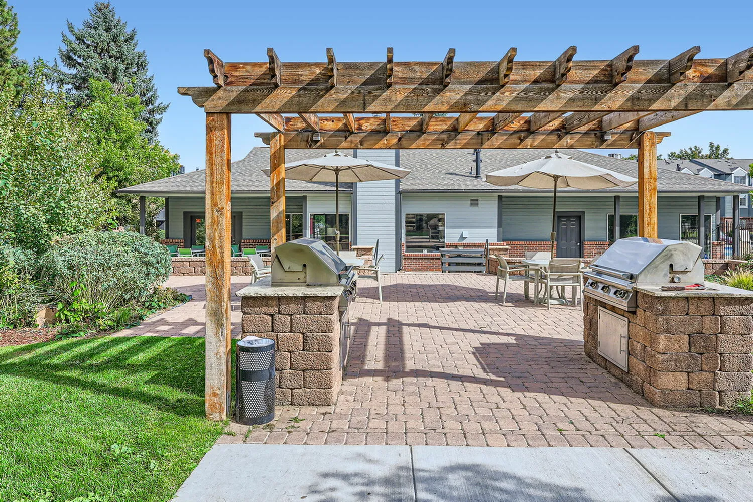 Inviting outdoor patio with a pergola, barbecue grills, and dining area surrounded by lush greenery.