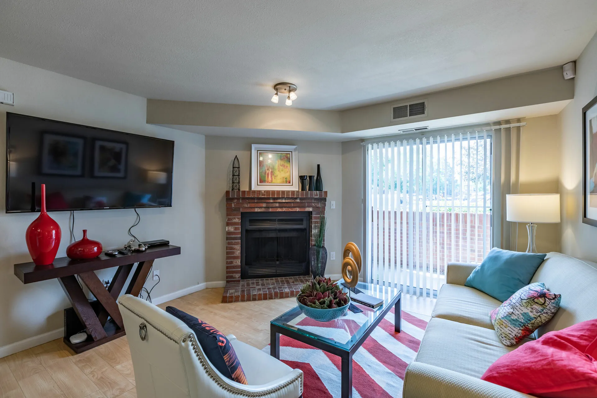 Inviting living room with modern decor featuring a cozy fireplace, sleek TV setup, and elegant furnishings accented by vibrant red and blue details.