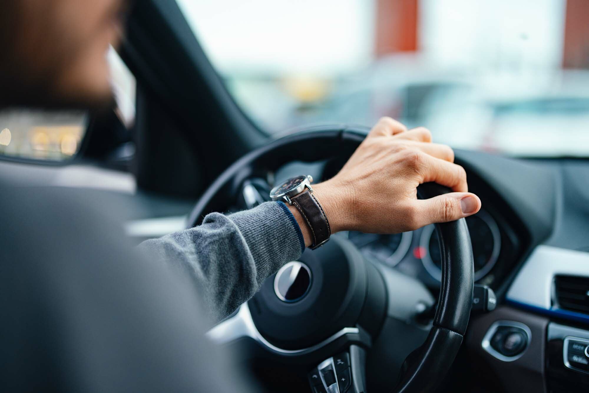 Close-up of a person driving a modern car, showcasing stylish interior and focus on the steering wheel.