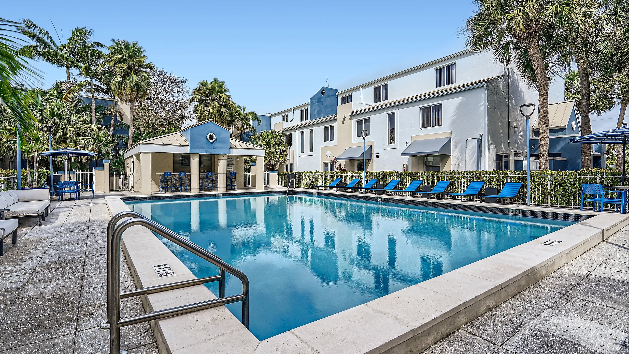 Elegant apartment complex featuring a pristine swimming pool, surrounded by lush palms and modern loungers.