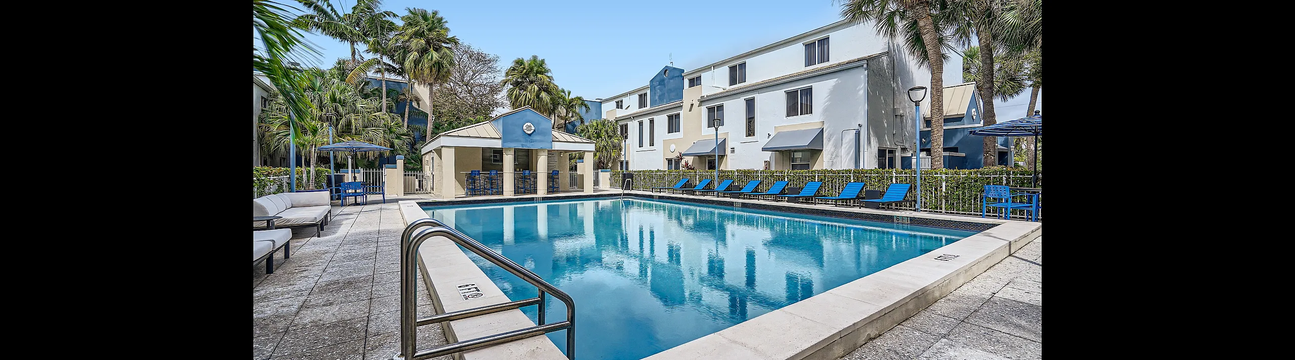 Inviting poolside oasis surrounded by lush palm trees and modern apartments, perfect for relaxation and leisure.