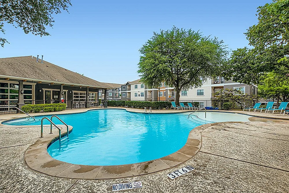 Inviting apartment complex pool with sun loungers, surrounded by lush greenery and modern buildings, perfect for relaxation.
