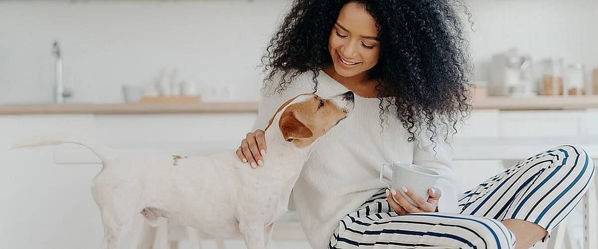 Cozy modern kitchen with a joyful woman enjoying coffee and bonding with her playful dog.