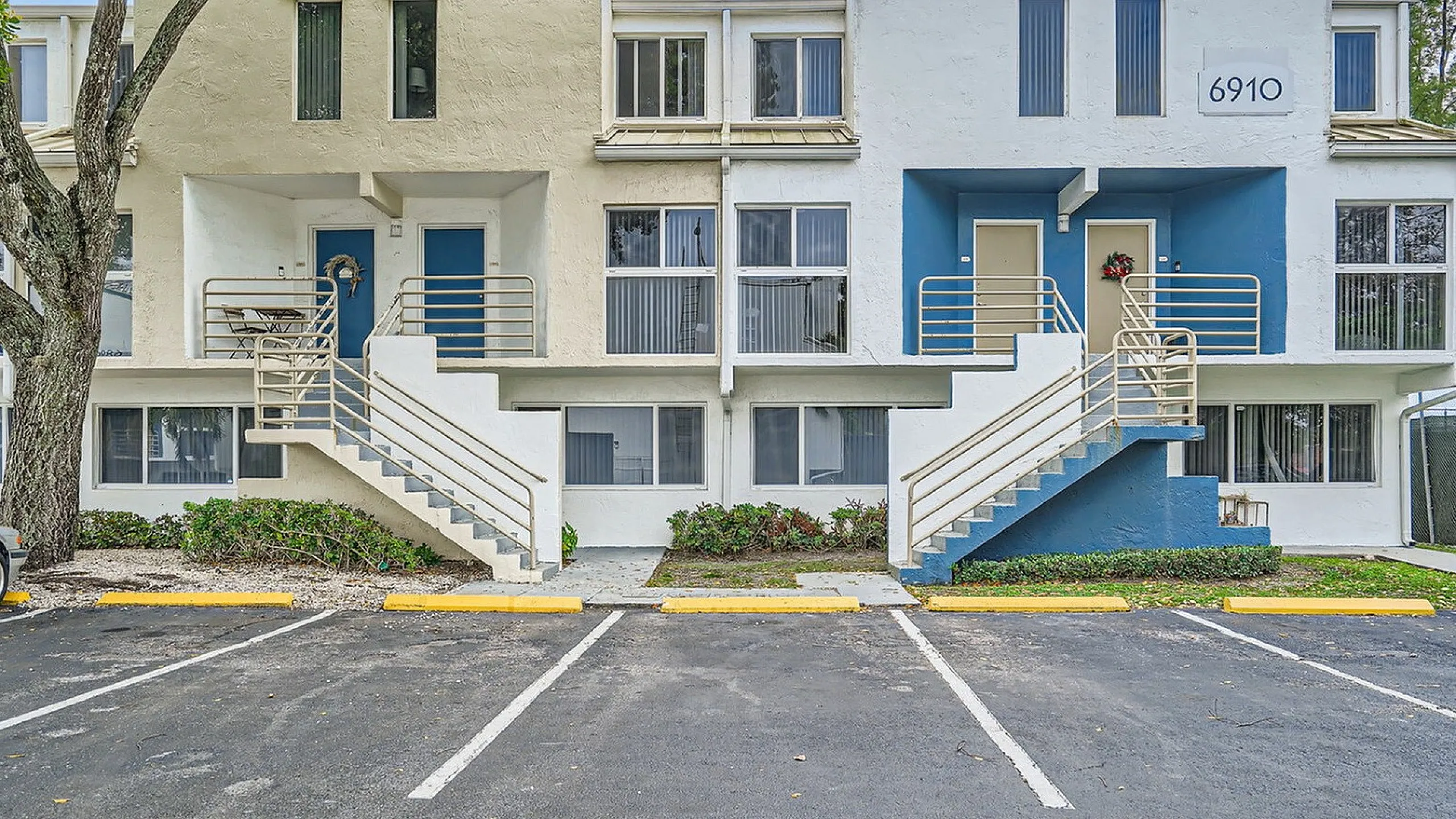 Charming townhouse exterior with dual staircases, vibrant blue accents, and well-manicured landscaping.