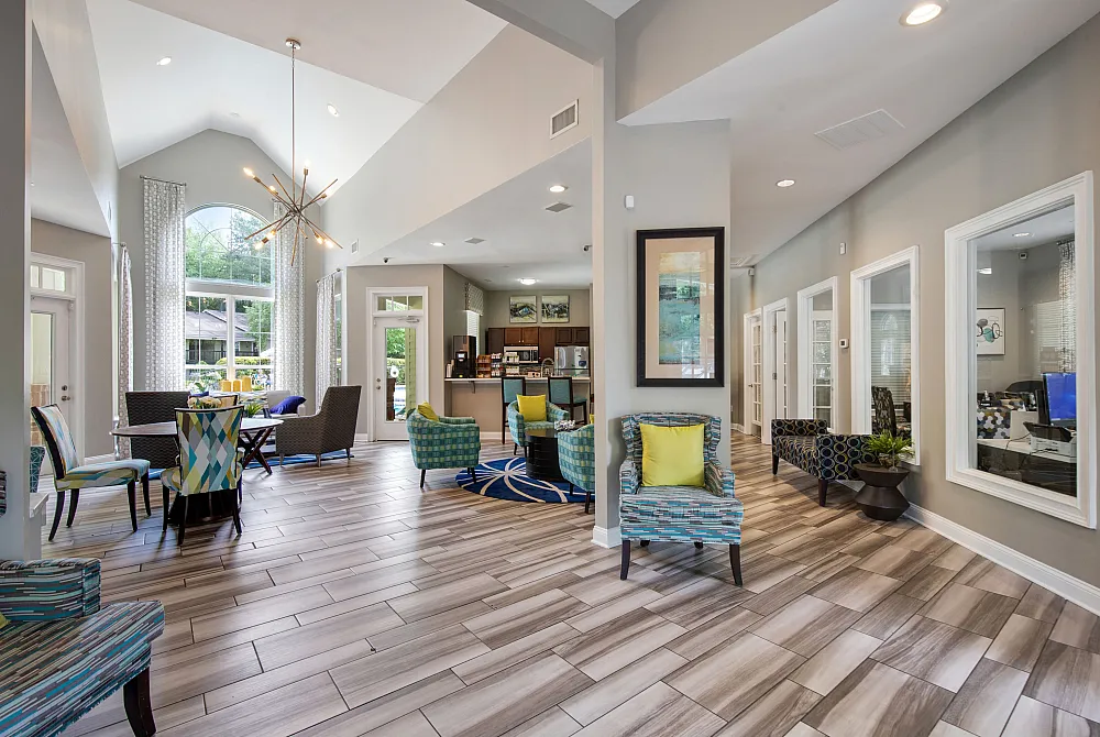 A residential lounge area with chairs, tables, meeting rooms, a kitchen area, and large windows at The Madison Charlotte, NC apartments.