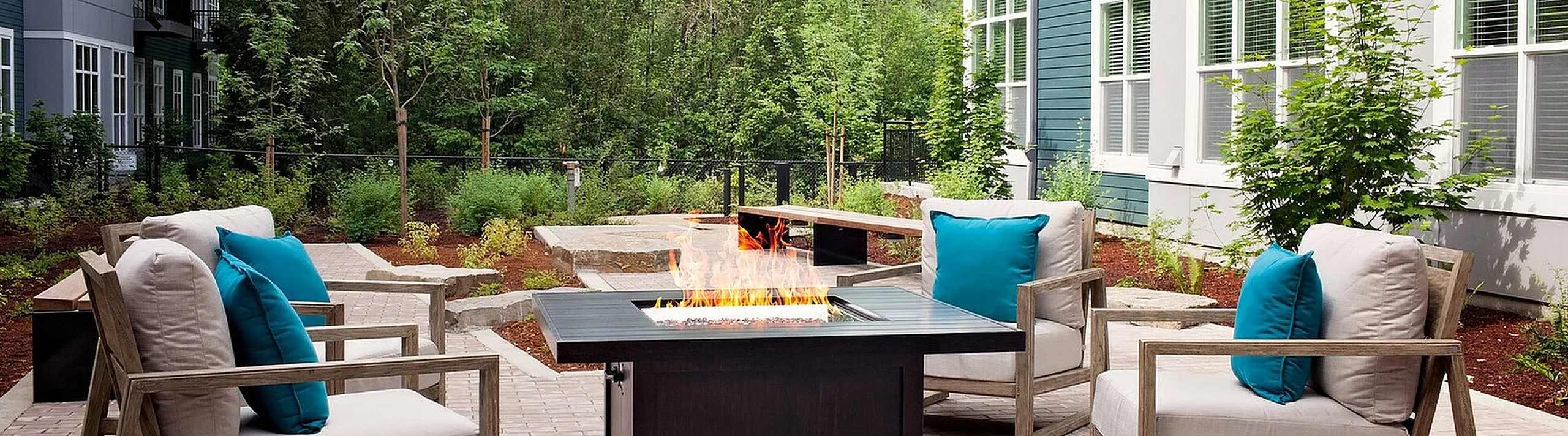 Charming outdoor patio with cozy seating and a modern fire pit, surrounded by lush greenery and stylish apartment architecture.