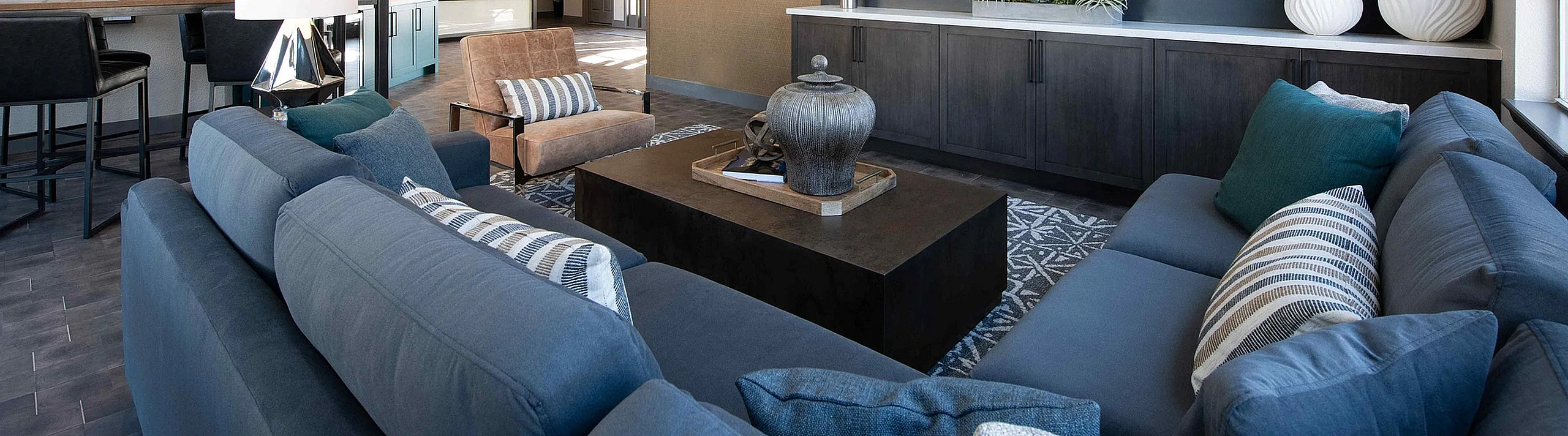 Modern living room with plush blue sofas, sleek black accent wall, and large flat screen TV. Elegant decor enhances the airy and inviting atmosphere.