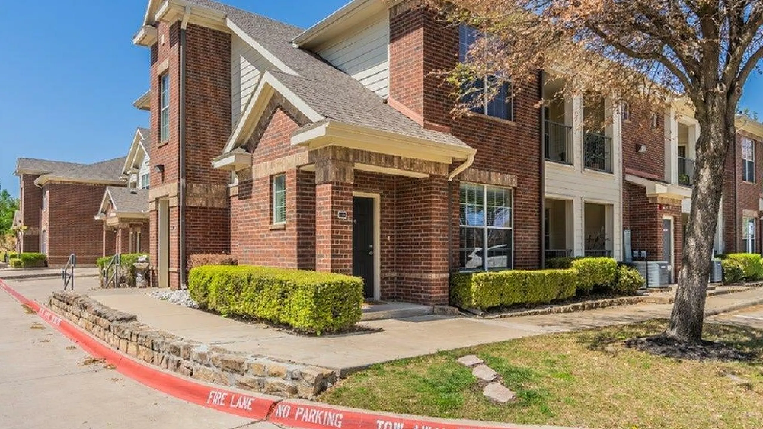 Charming red-brick apartment building with beautiful landscaping, showcasing a modern and inviting exterior on a sunny day.