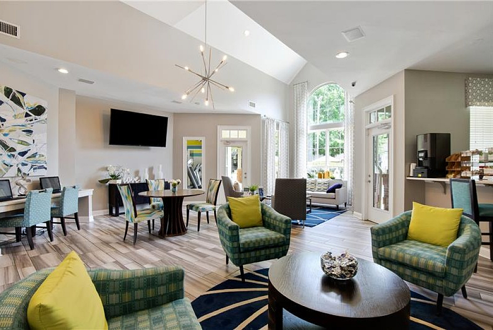 A residential lounge area with chairs, tables, a flatscreen television, and large windows at The Madison apartments for rent in Charlotte, North Carolina.