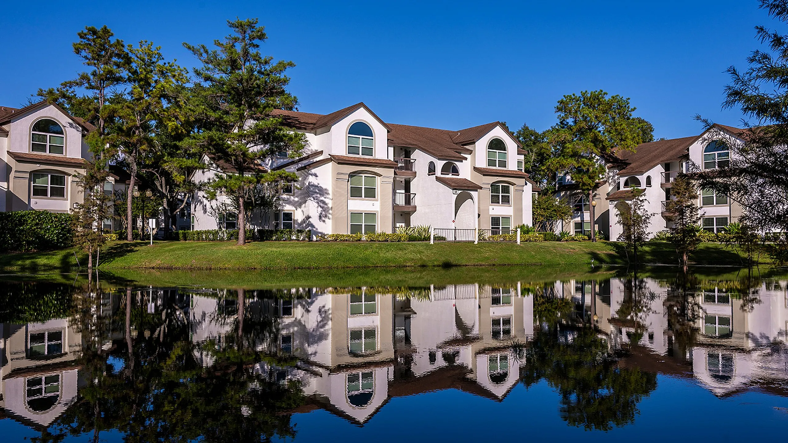 Charming residential building nestled among lush trees and palm-lined paths, bathed in warm sunlight.