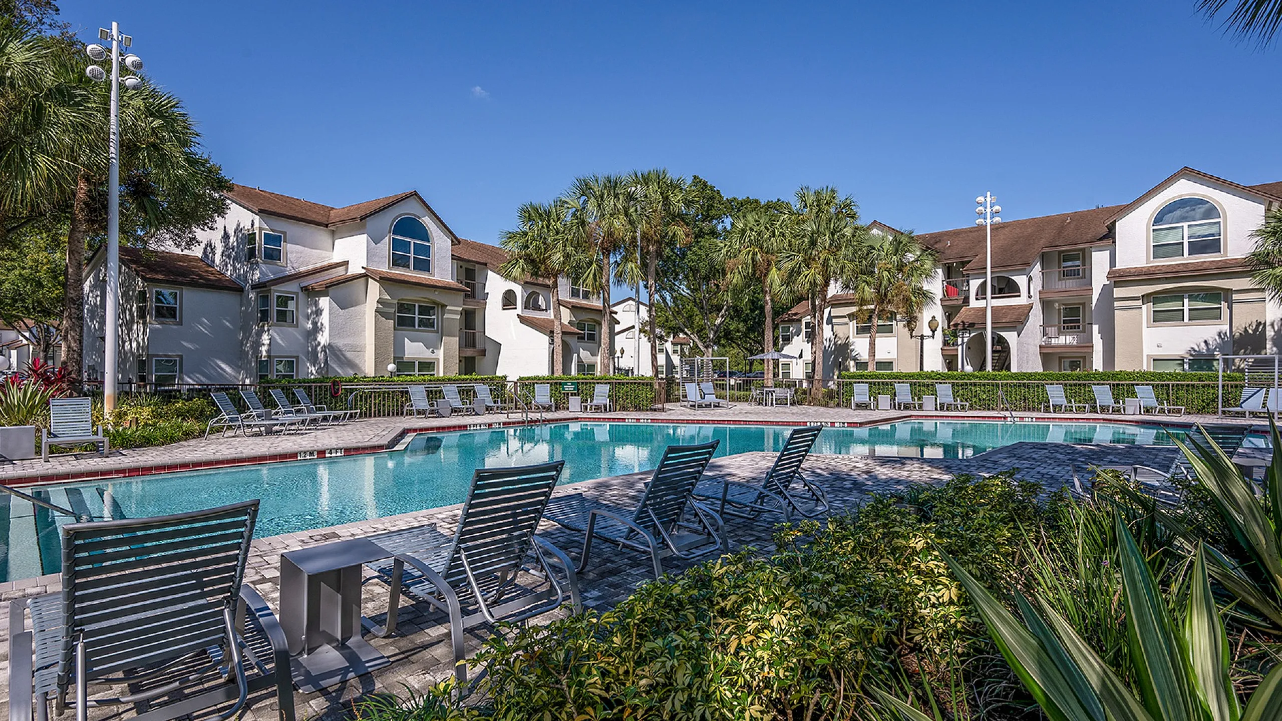Inviting outdoor pool area with modern clubhouse under a bright blue sky, perfect for relaxation and leisure.