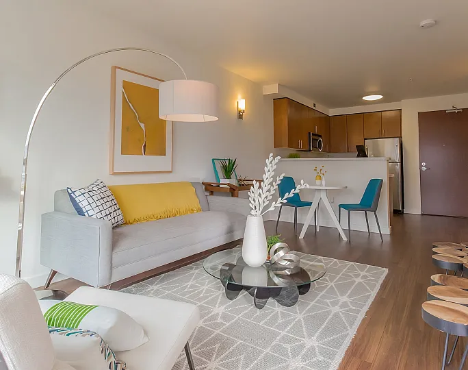 Bright and modern living room with large windows, stylish decor, and a cozy gray sofa on a patterned rug.