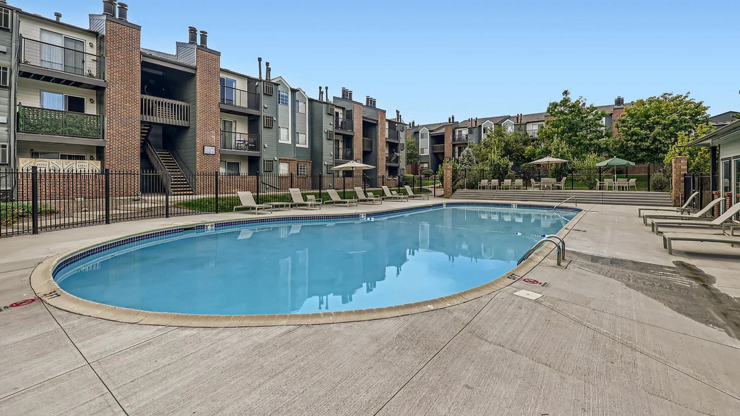 Inviting outdoor pool area with sun loungers, surrounded by modern apartment buildings and lush greenery.