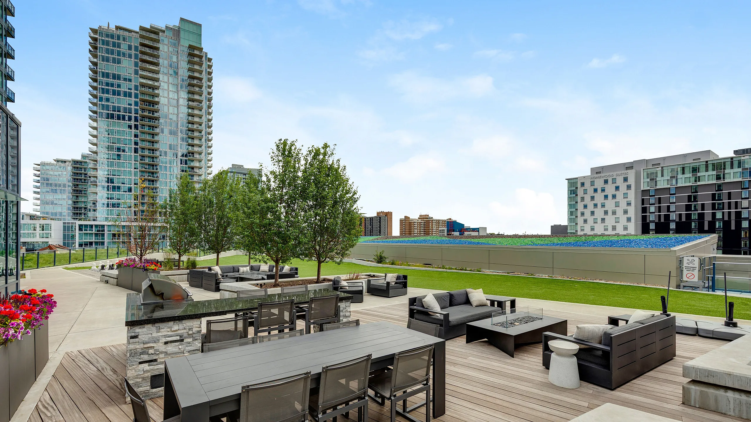 Modern urban rooftop terrace with stylish outdoor seating, lush greenery, and vibrant city view.