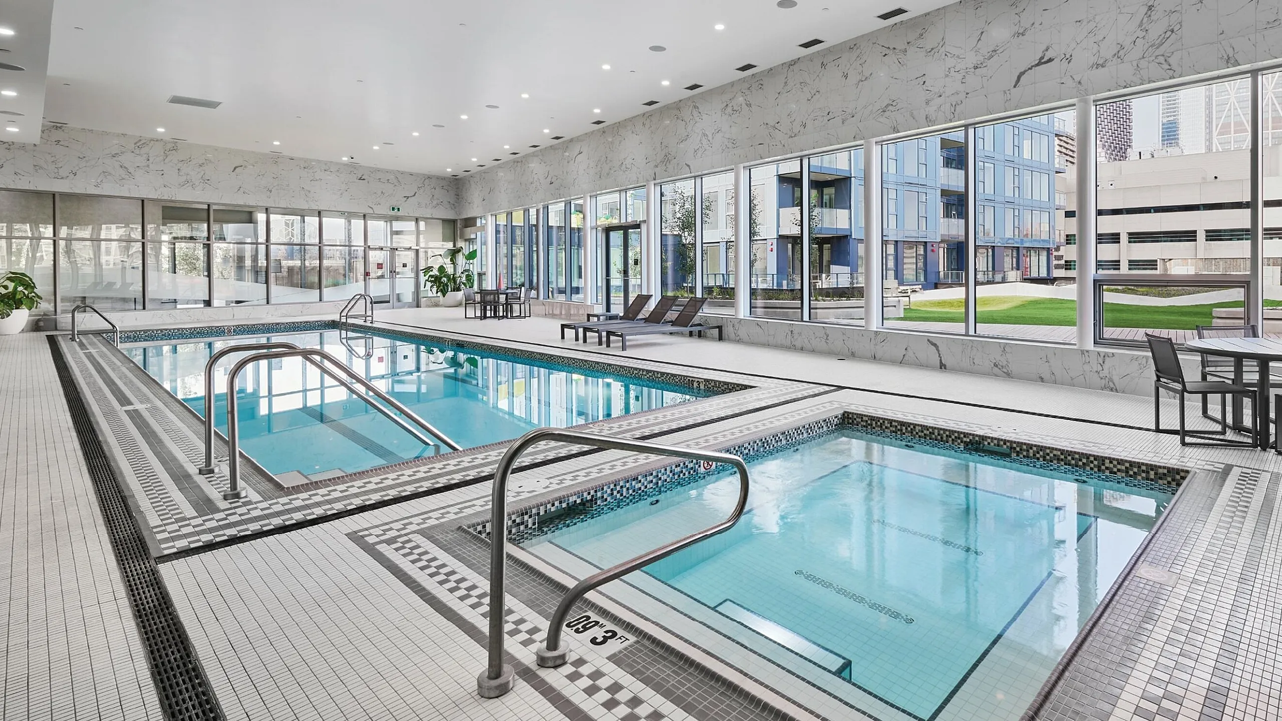 Luxurious indoor pool area with floor-to-ceiling windows, offering a modern and relaxing environment with lounge chairs and stylish decor.