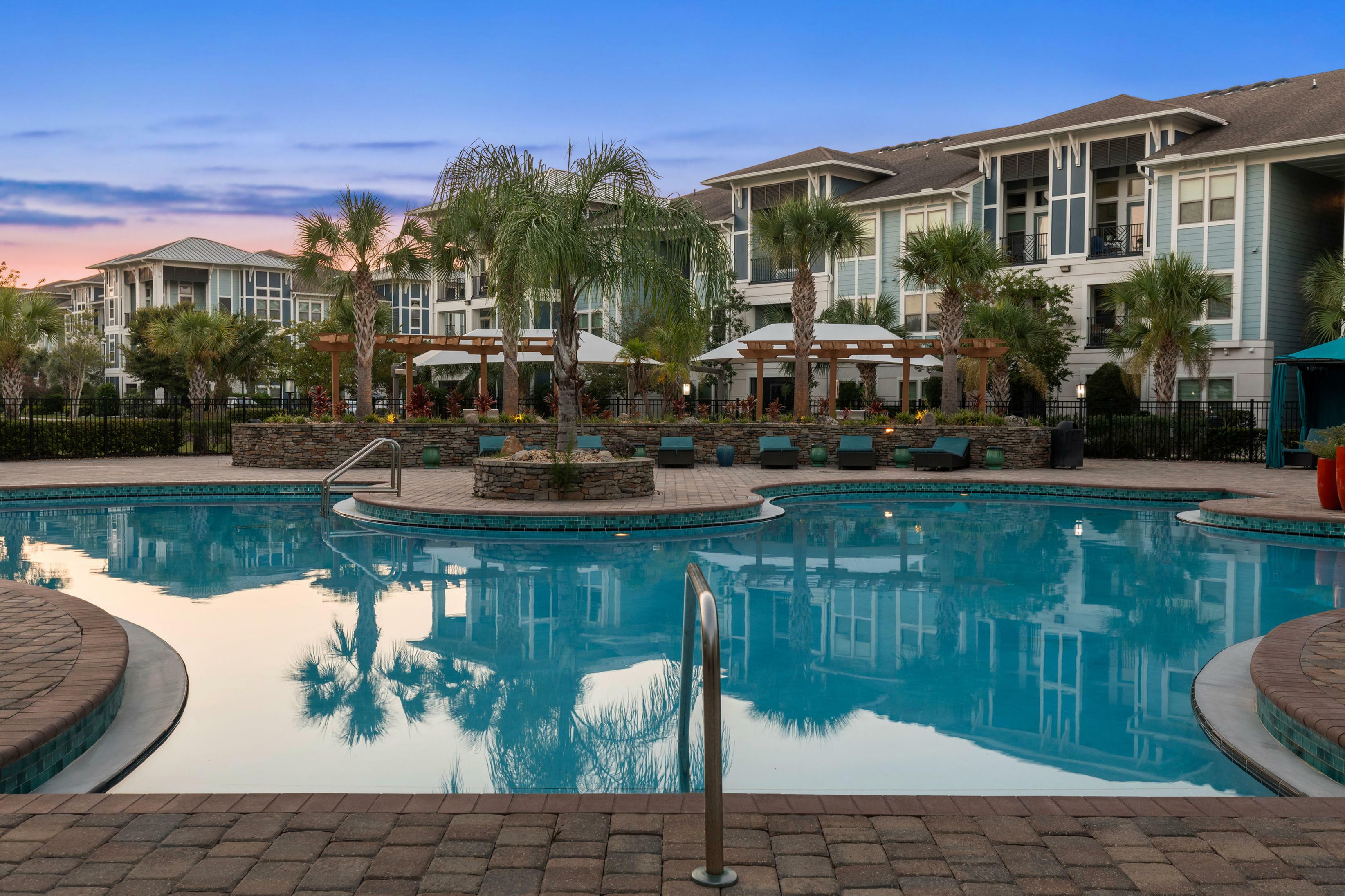 Luxurious apartment complex showcasing a stunning resort-style pool surrounded by lush palm trees and elegant lounge areas.