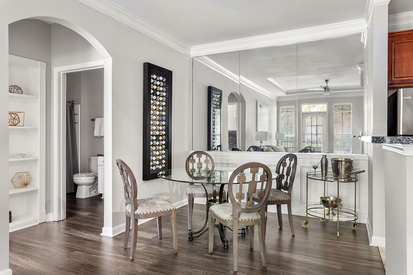 Elegant dining area with stylish glass table and mirrored wall, showcasing modern decor and warm wood flooring.