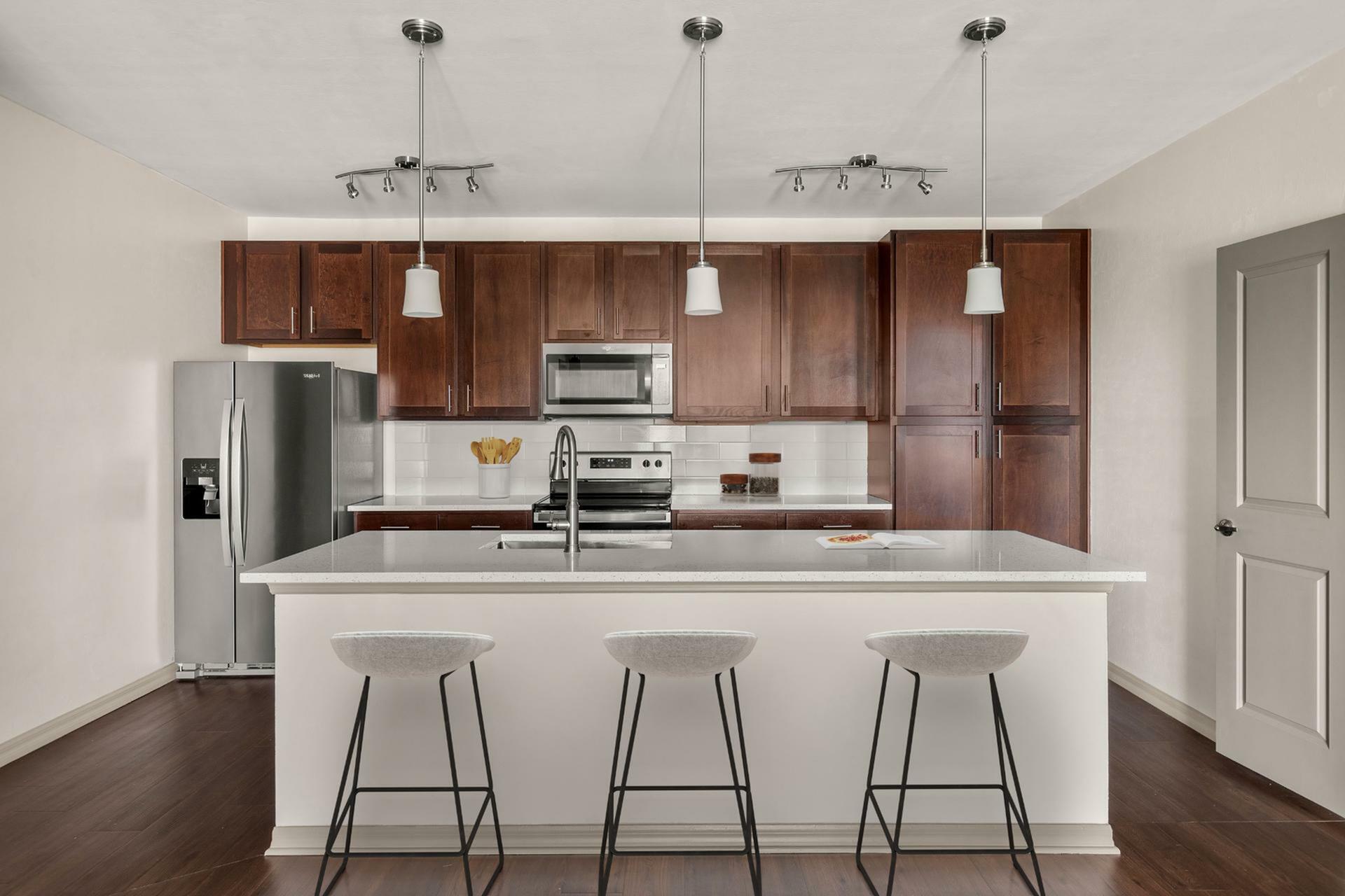 Modern kitchen with rich wood cabinetry, stainless steel appliances, and a sleek island with contemporary pendant lighting.