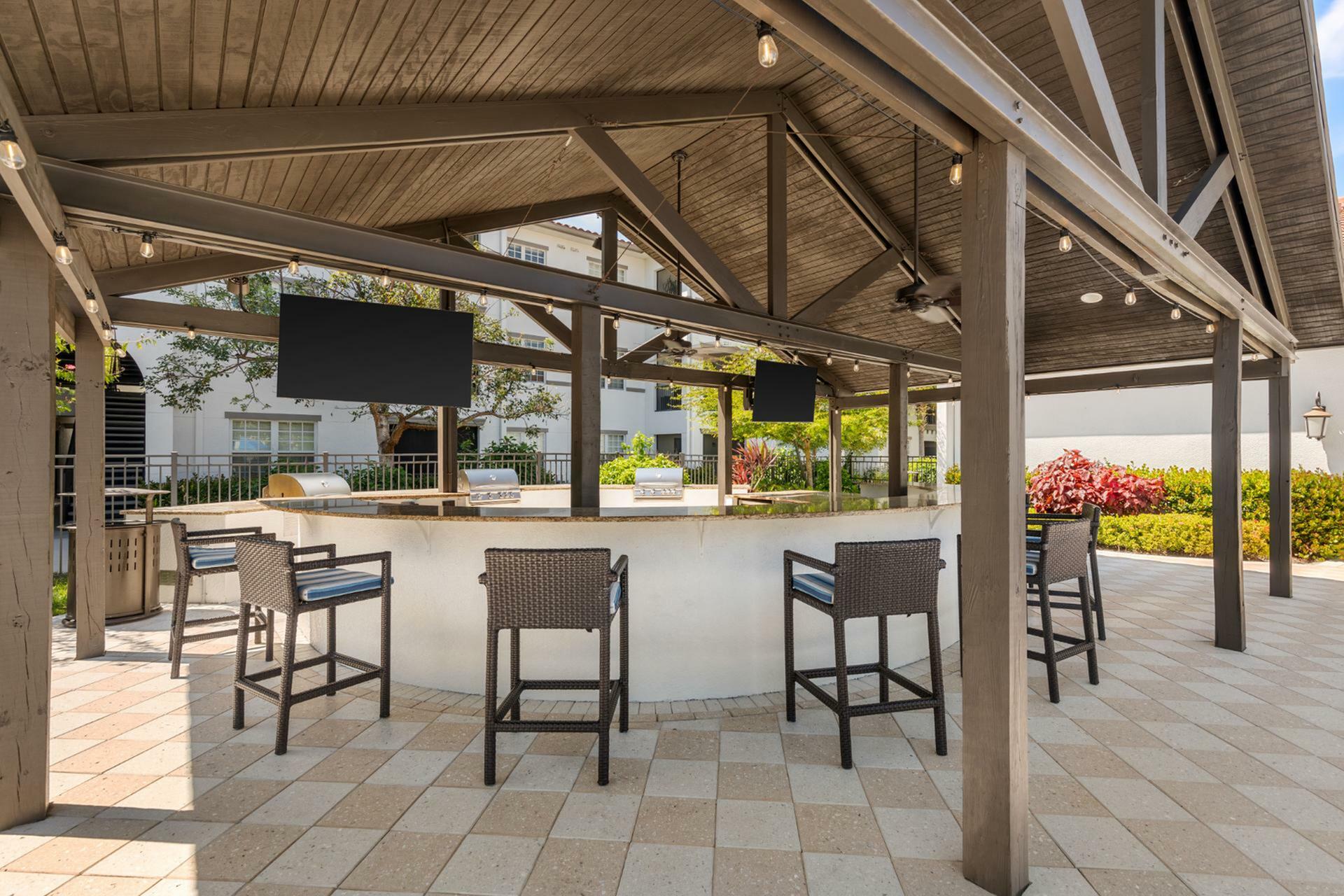 Chic outdoor entertainment area featuring stylish bar seating, dual grills, and ambient string lighting under a sleek pavilion.