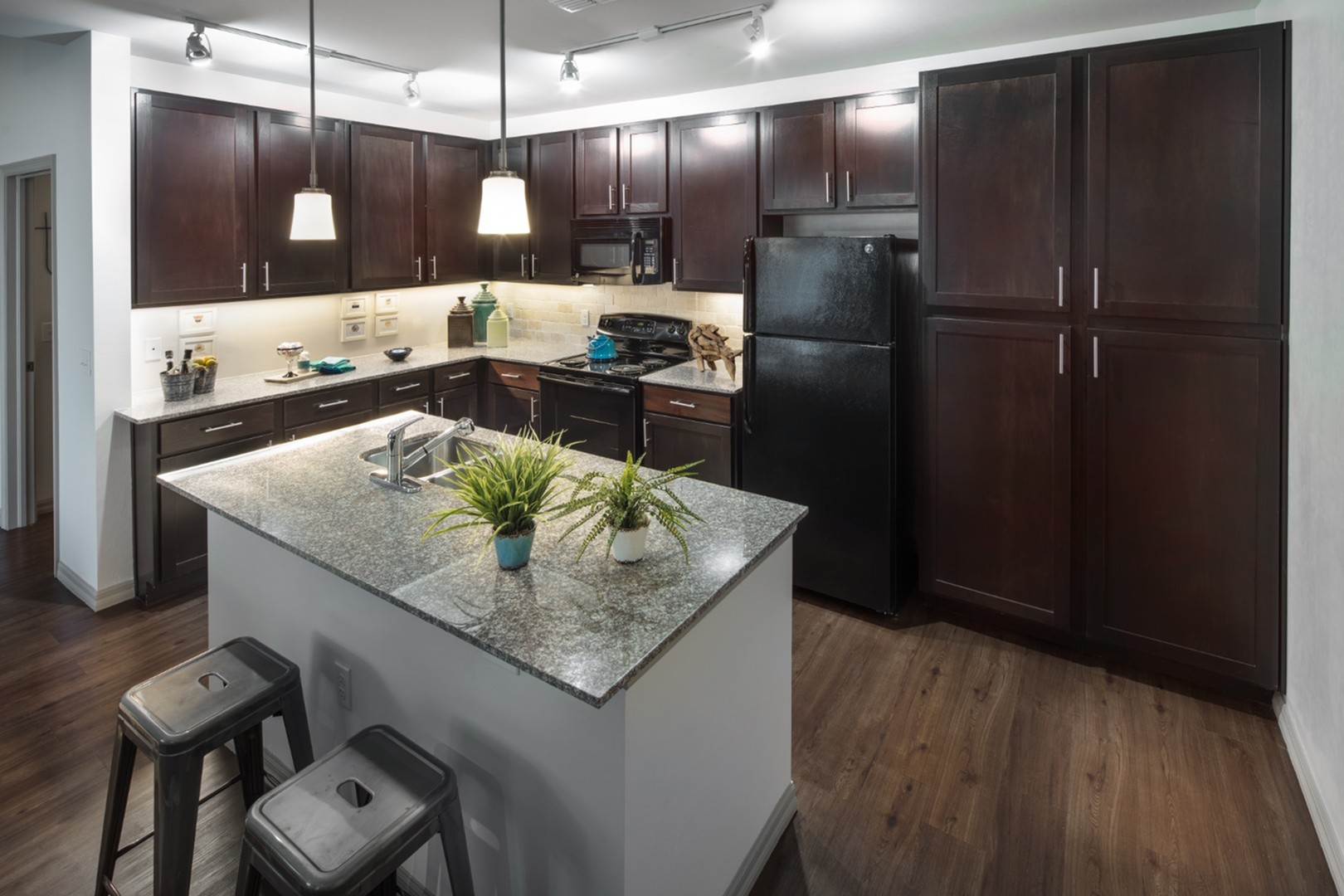 Modern kitchen boasting elegant dark wood cabinets, sleek granite countertops, and stainless steel appliances under warm pendant lighting.