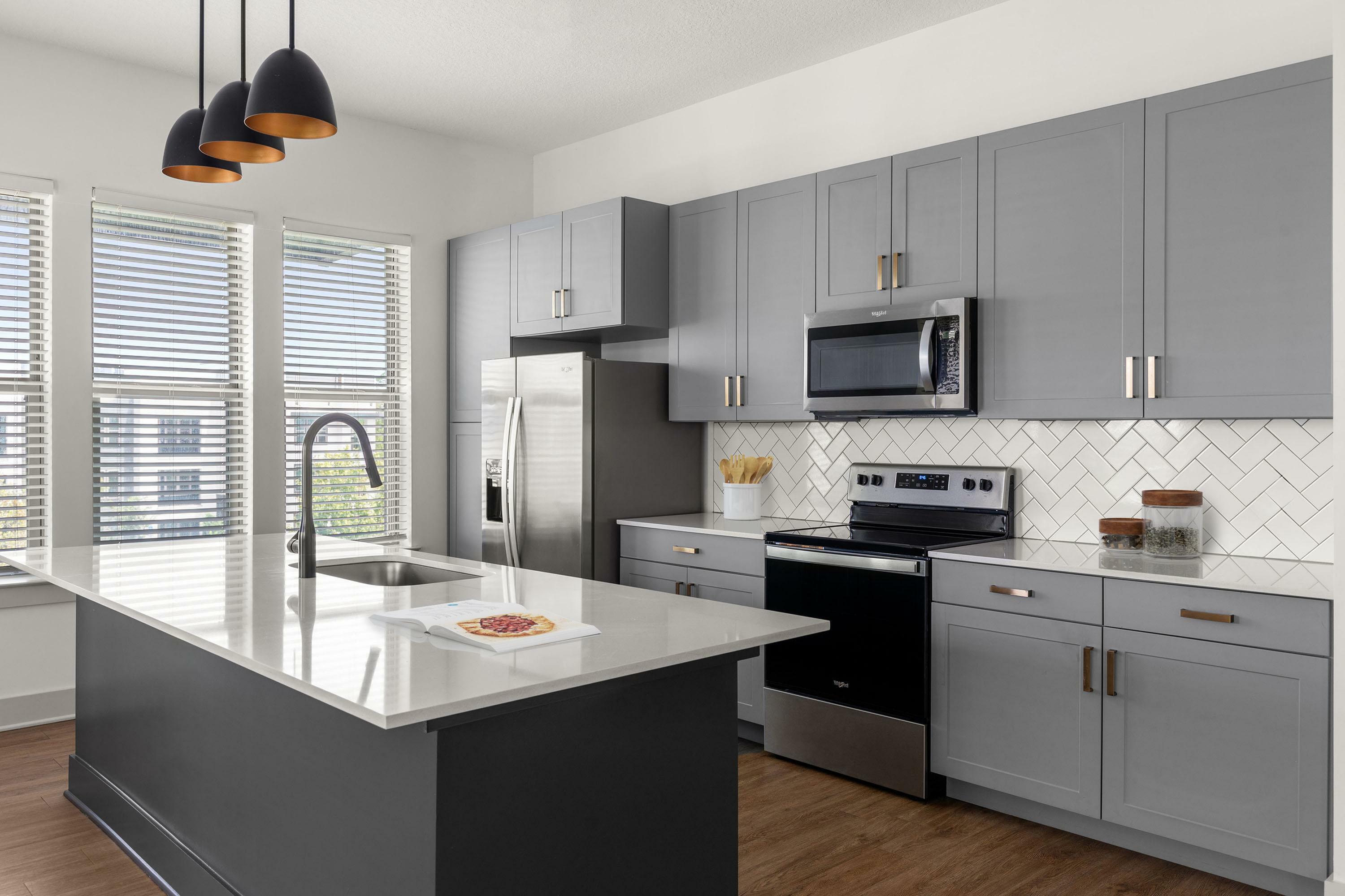 Modern kitchen with sleek gray cabinets, stainless steel appliances, and a spacious island with elegant pendant lighting.