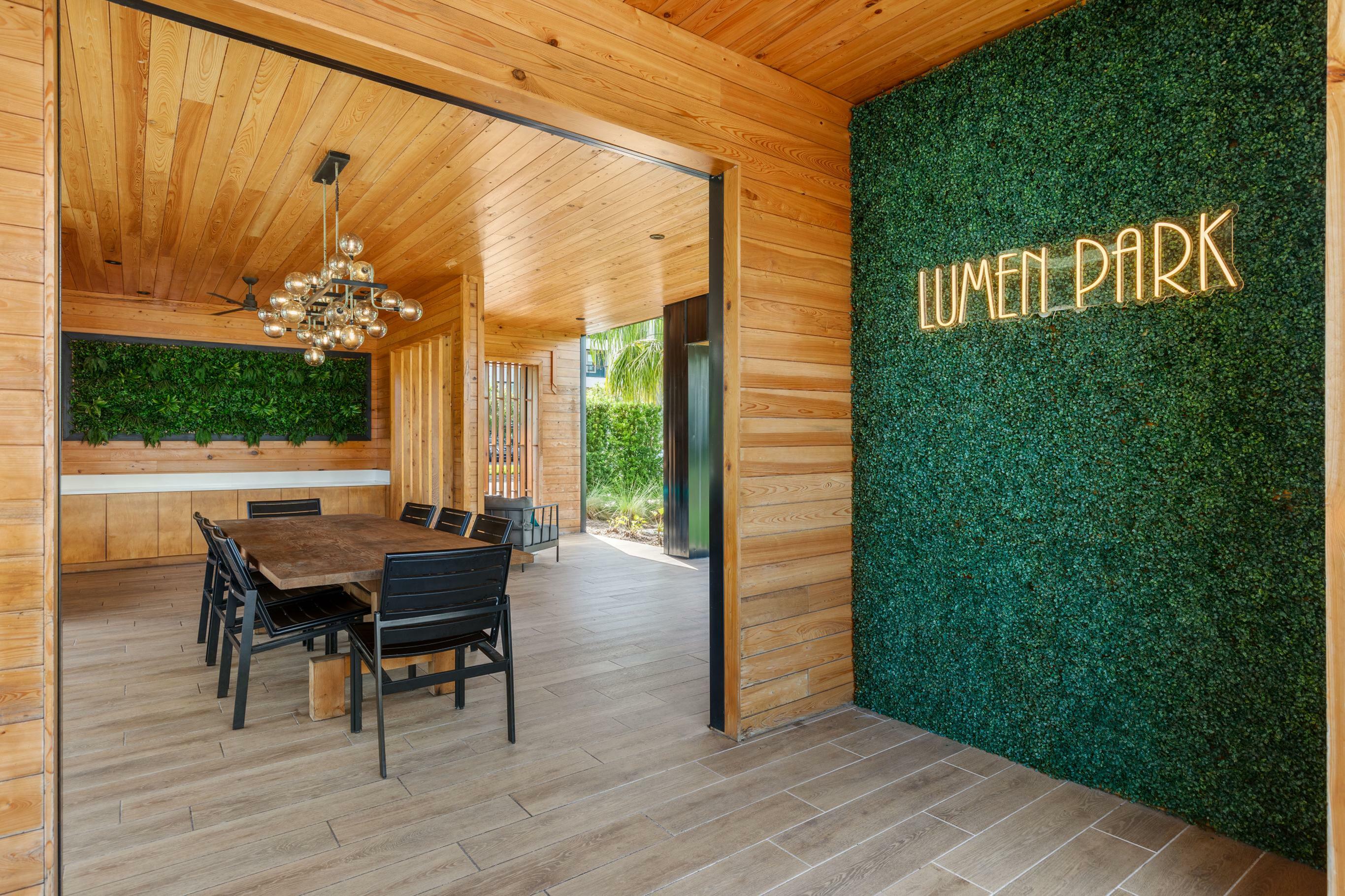 Chic dining area in Lumen Park with elegant wooden design and lush green wall, perfect for gatherings.