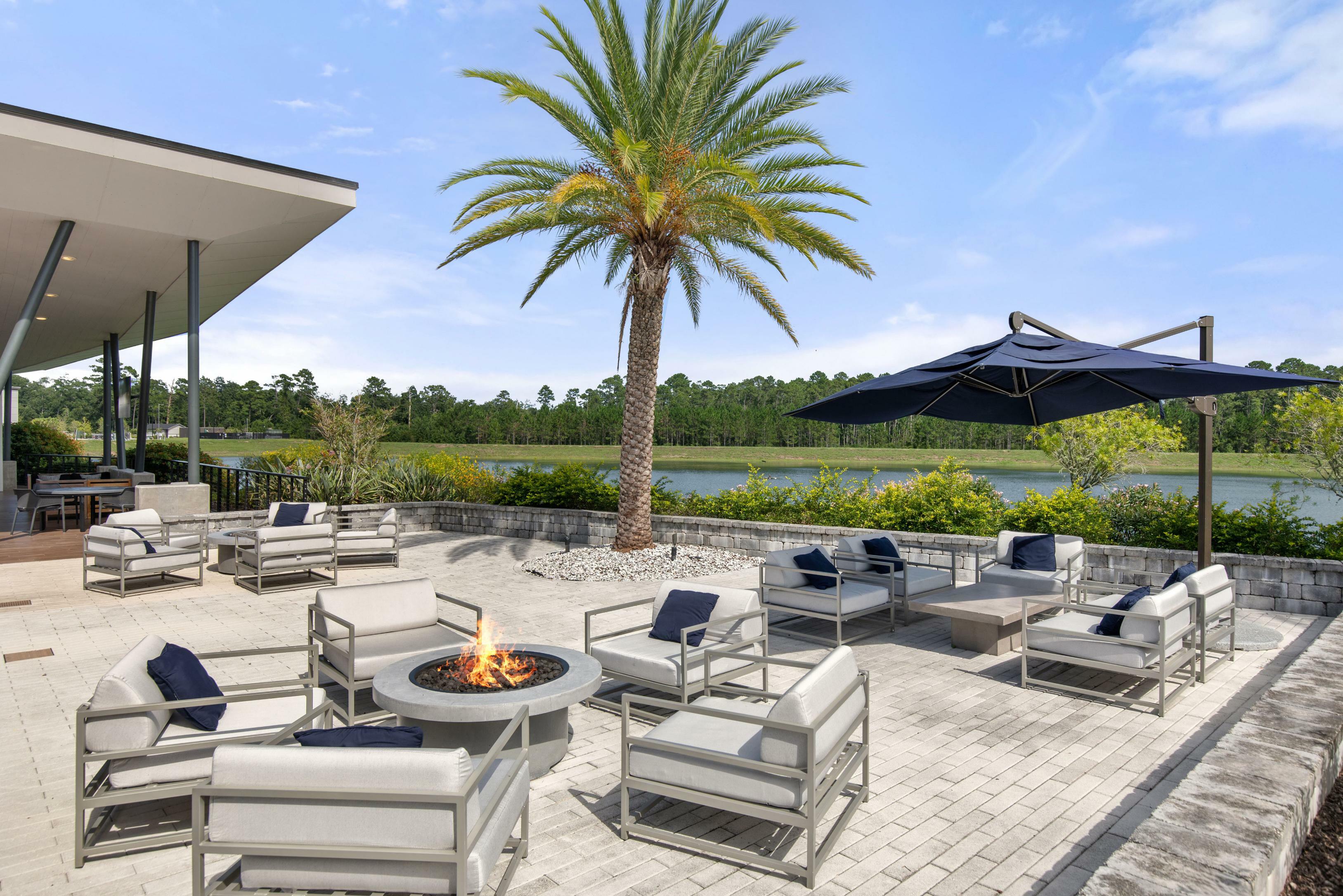 Luxurious outdoor patio with comfortable seating, cozy fire pit, and stunning lakeside view under a clear blue sky.
