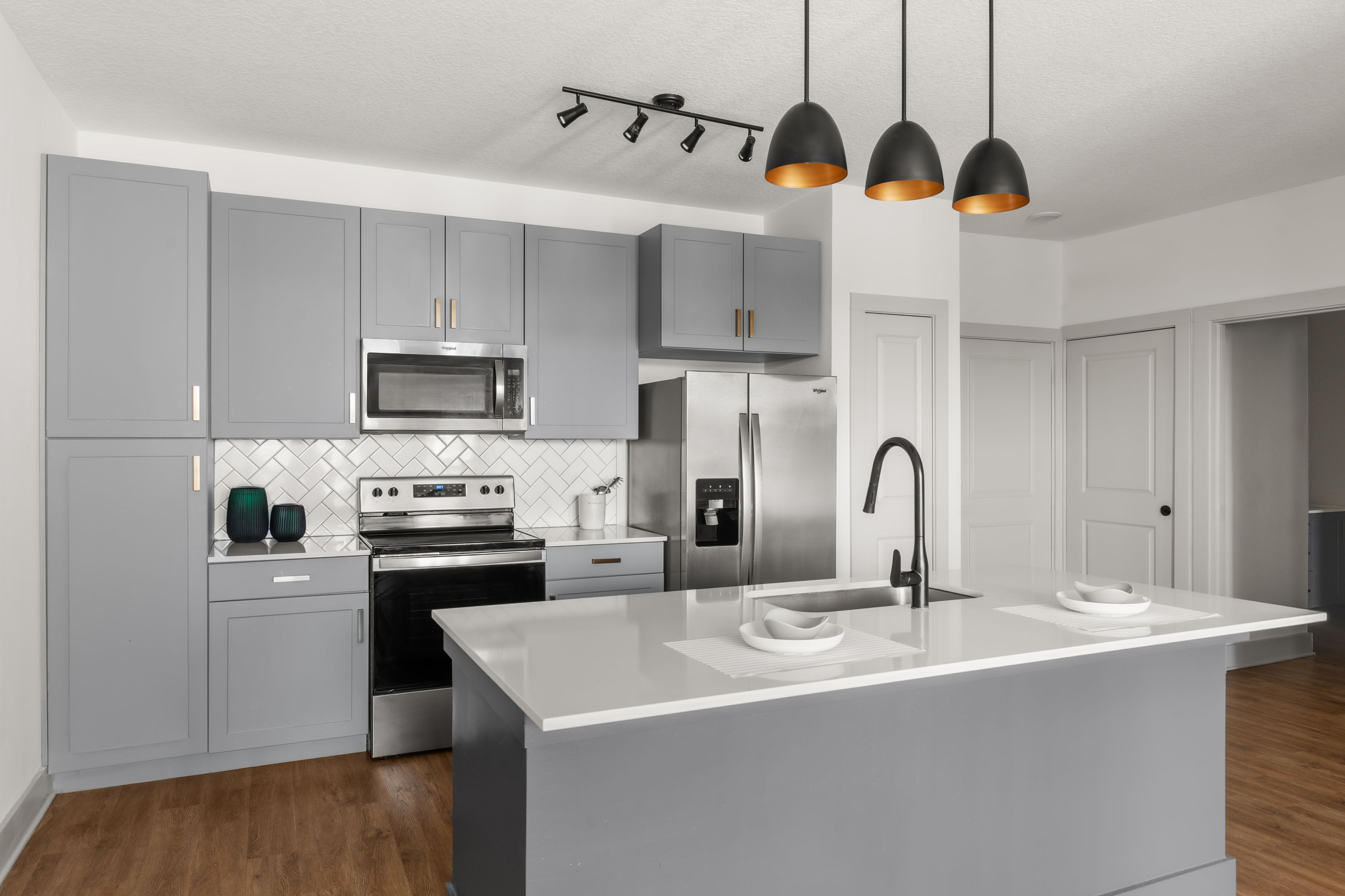 Modern kitchen with sleek gray cabinetry, stainless steel appliances, and an elegant island with pendant lighting.