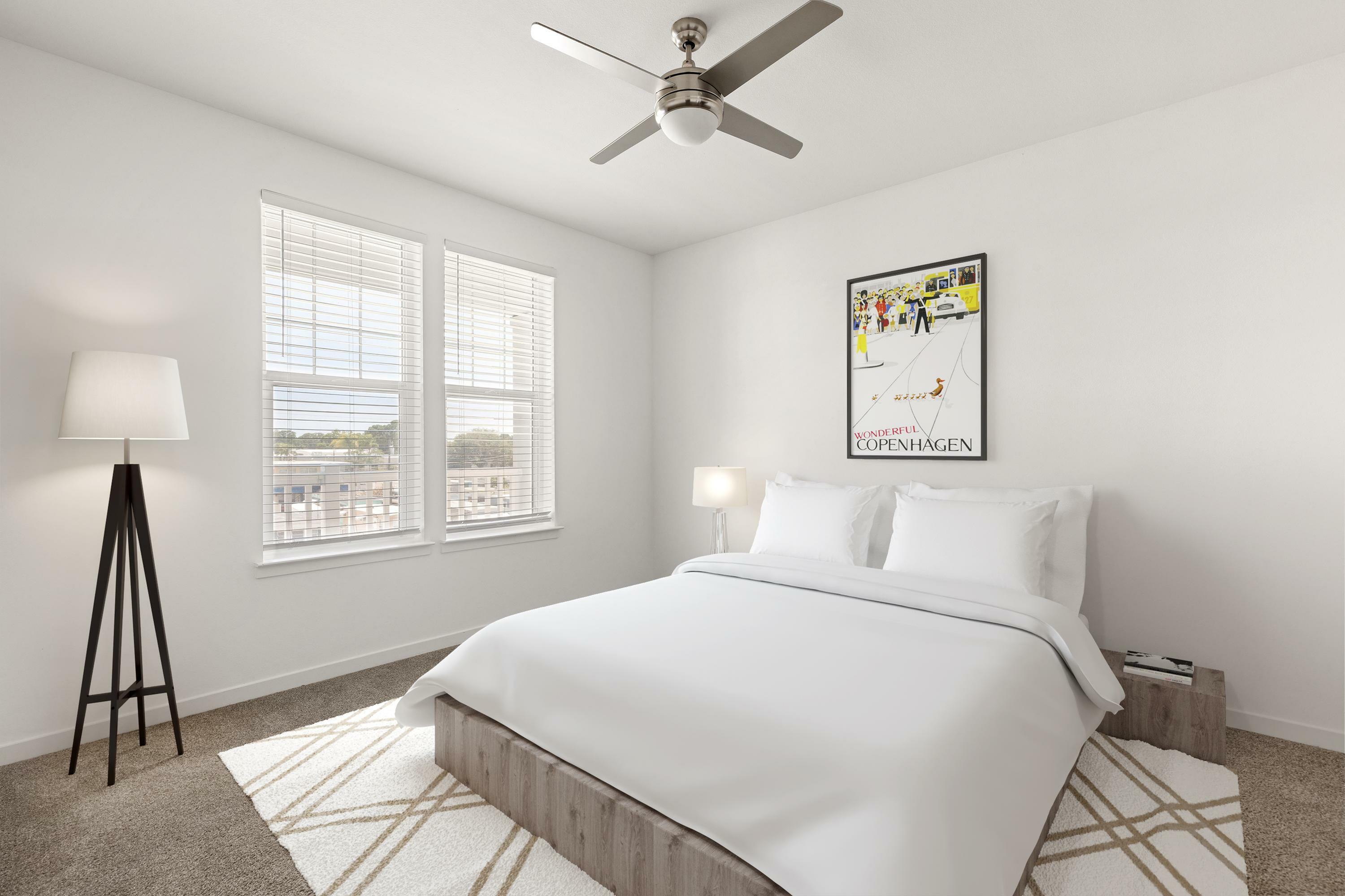Bright and inviting bedroom with a stylish ceiling fan, modern furnishings, and ample natural light from large windows.