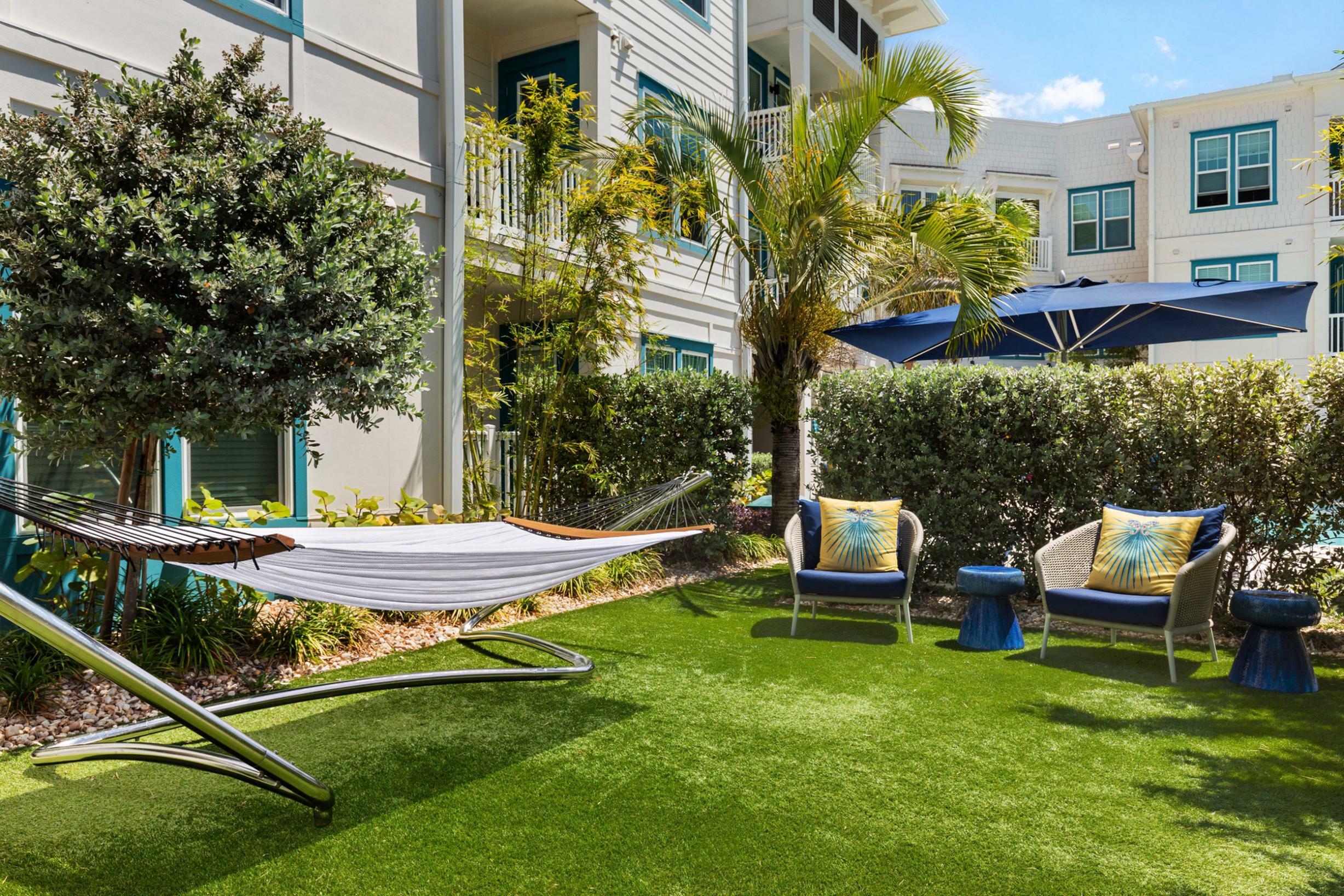 Charming outdoor space with hammock and cozy seating, surrounded by lush greenery in a modern apartment community.