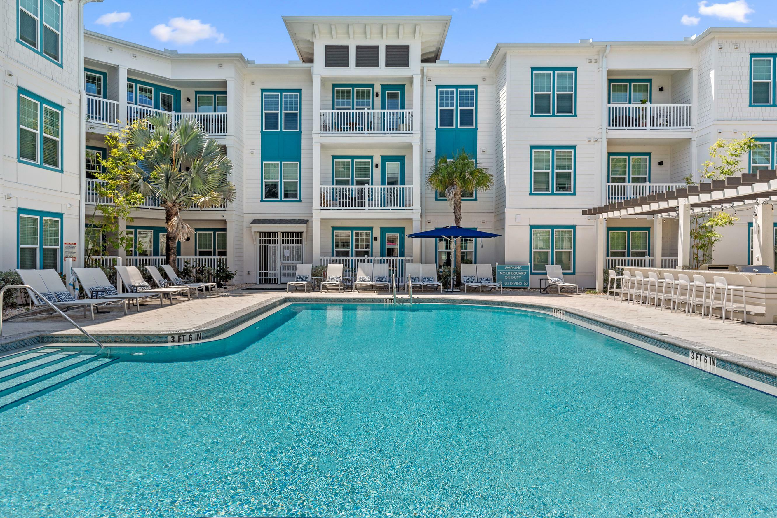 Luxurious apartment complex with a sparkling pool, surrounded by modern architecture and inviting outdoor seating.