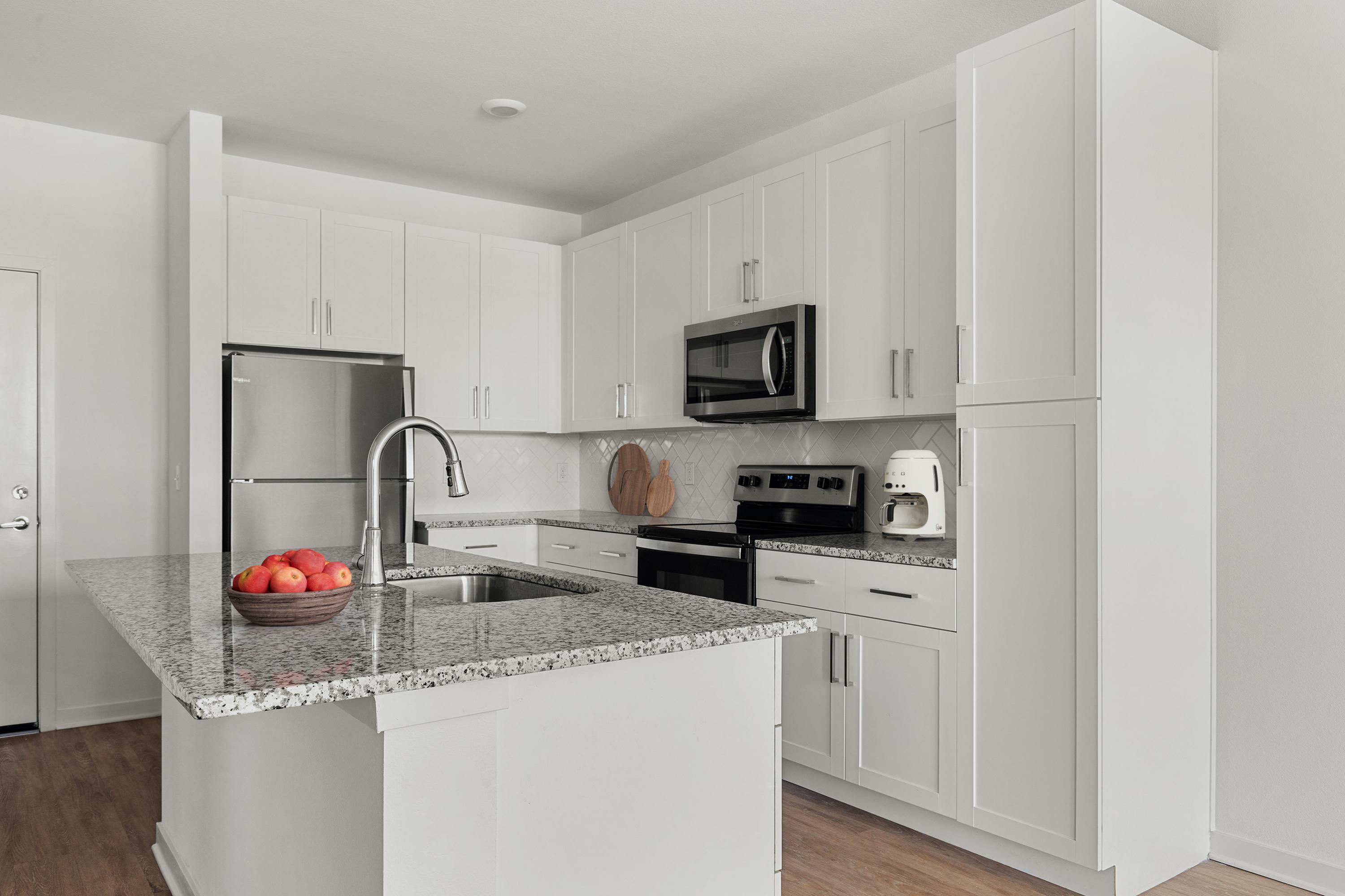 Modern kitchen featuring sleek white cabinetry, granite countertops, and stainless steel appliances.