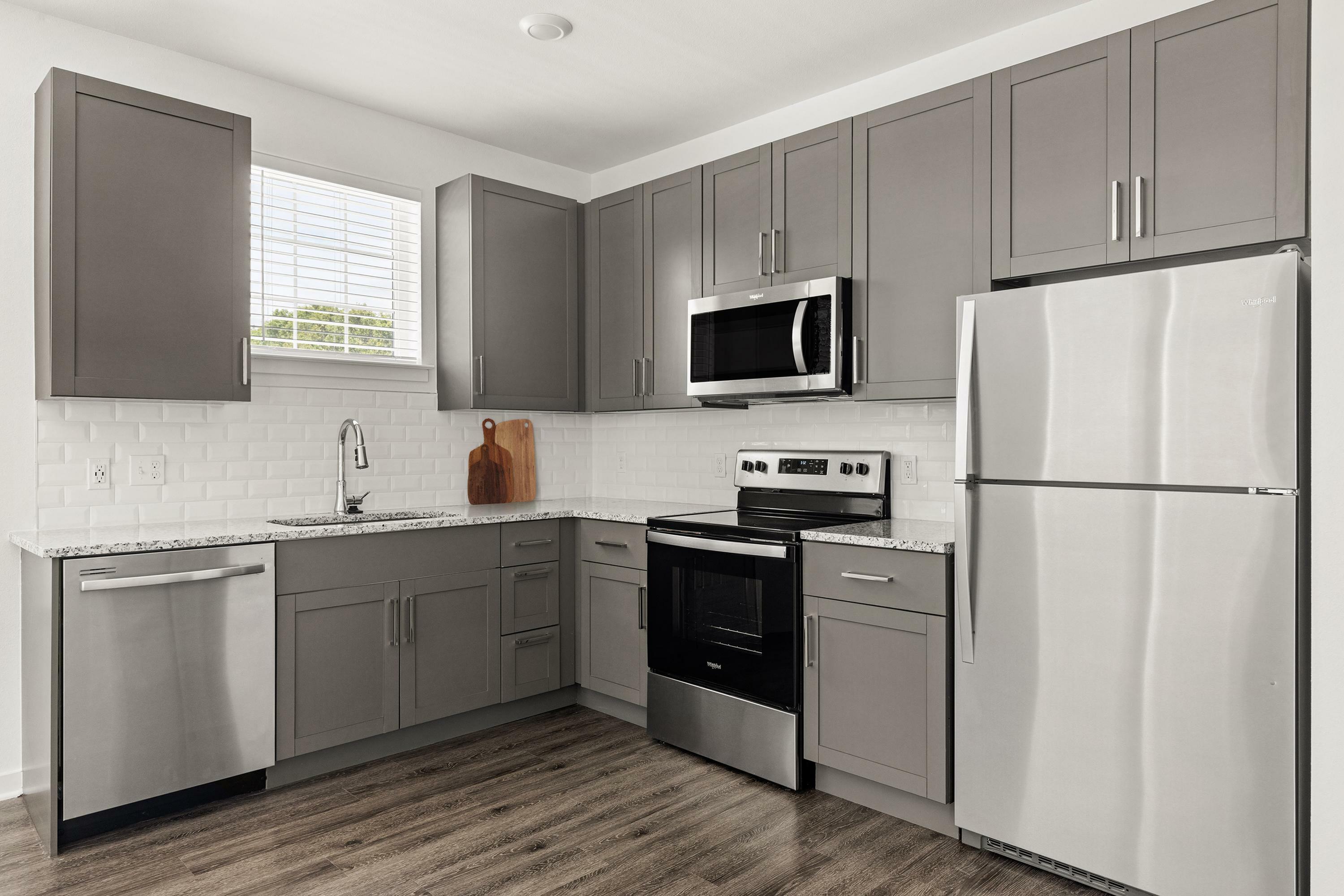 Modern kitchen with sleek gray cabinetry, stainless steel appliances, granite countertops, and hardwood floors.