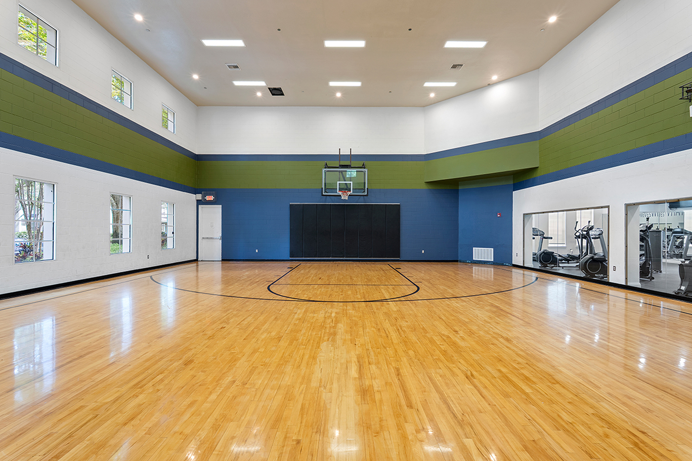 Spacious indoor basketball court with polished hardwood floors, vibrant wall accents, and ample natural light.
