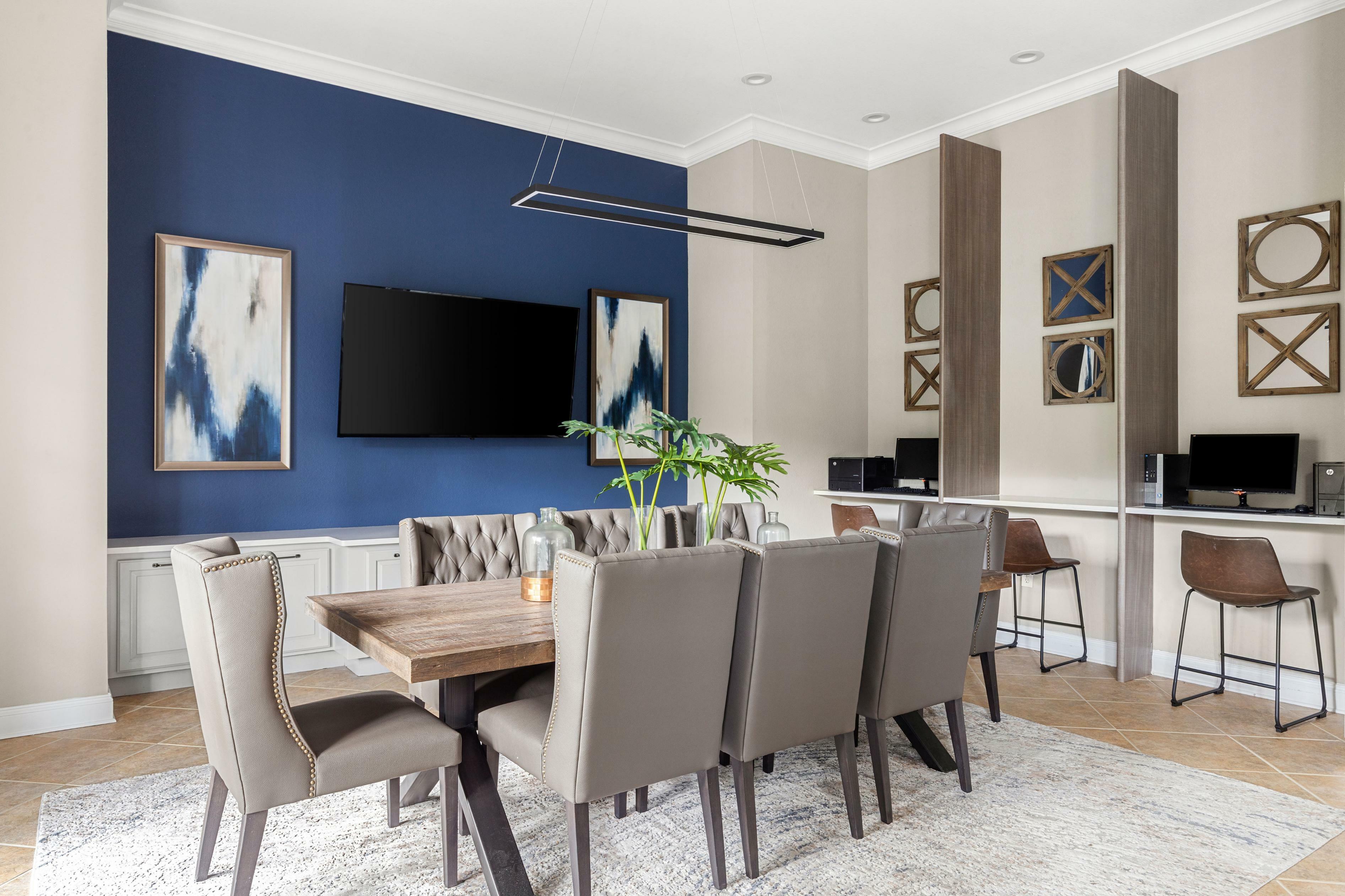 Elegant apartment dining and work area with modern decor, featuring a chic wooden table, plush chairs, and a stylish navy accent wall with contemporary art.
