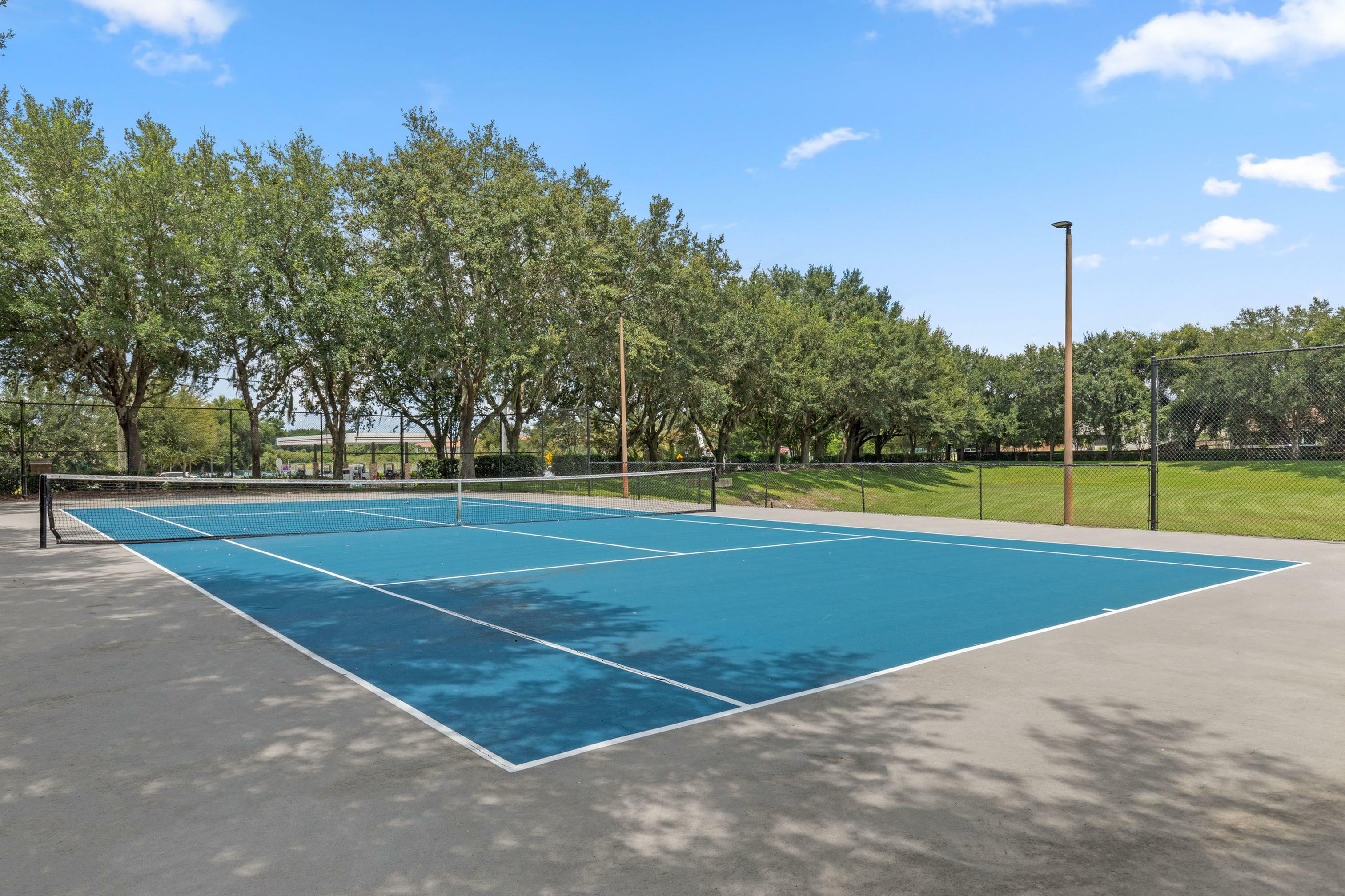 Inviting outdoor tennis court surrounded by lush green trees on a sunny day, perfect for recreational activities and relaxation.