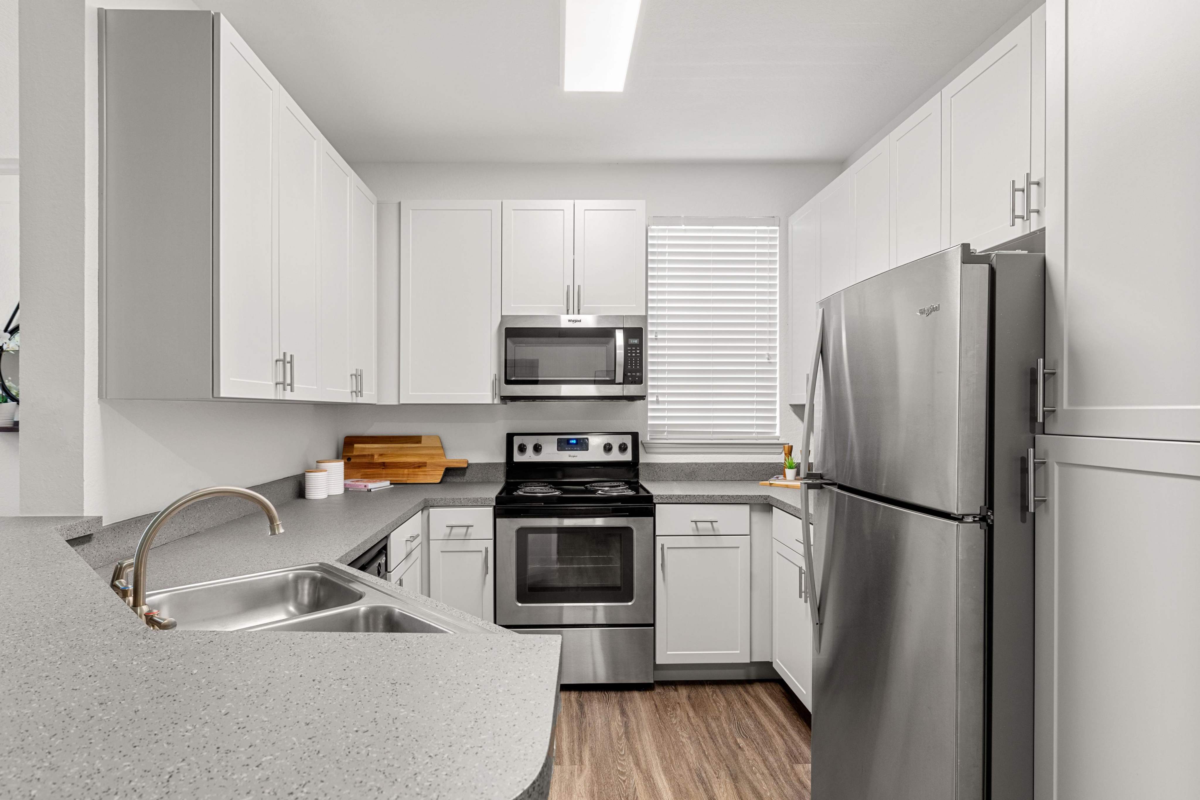 Modern kitchen with sleek stainless steel appliances, ample white cabinetry, and elegant gray countertops, featuring a convenient double sink and abundant natural light.